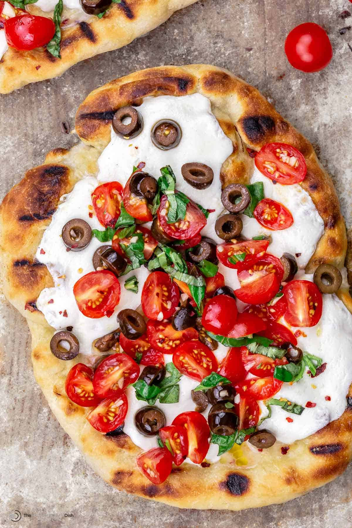 Pizza 桌布 壁紙 — 新鮮出爐的扁麵包披薩，上面鋪滿奶油白起司、櫻桃番茄、黑橄欖和羅勒葉。