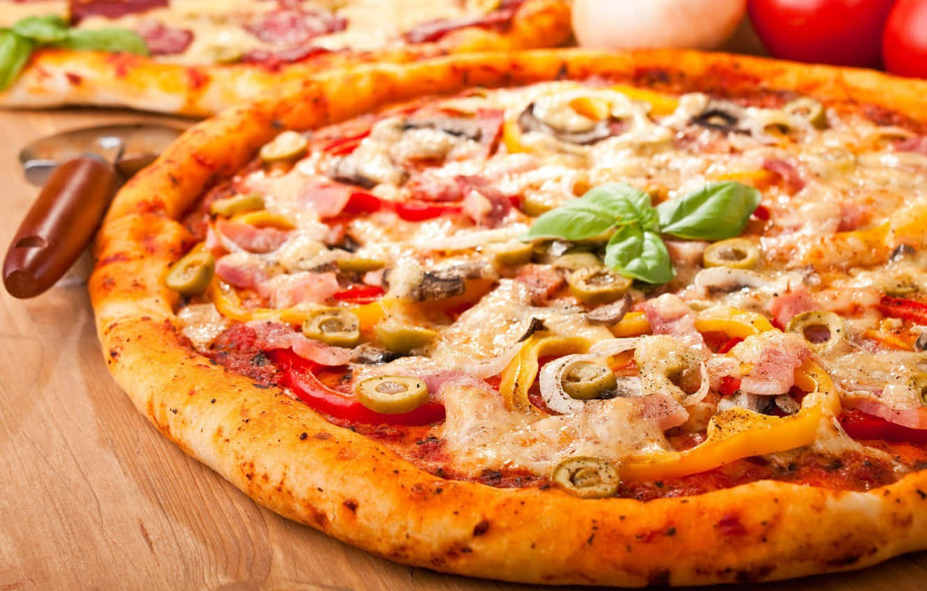 Pizza 桌布 壁紙 — 新鮮出爐的披薩，上面有橄欖、甜椒、火腿和羅勒，放在木板上，旁邊有披薩刀。