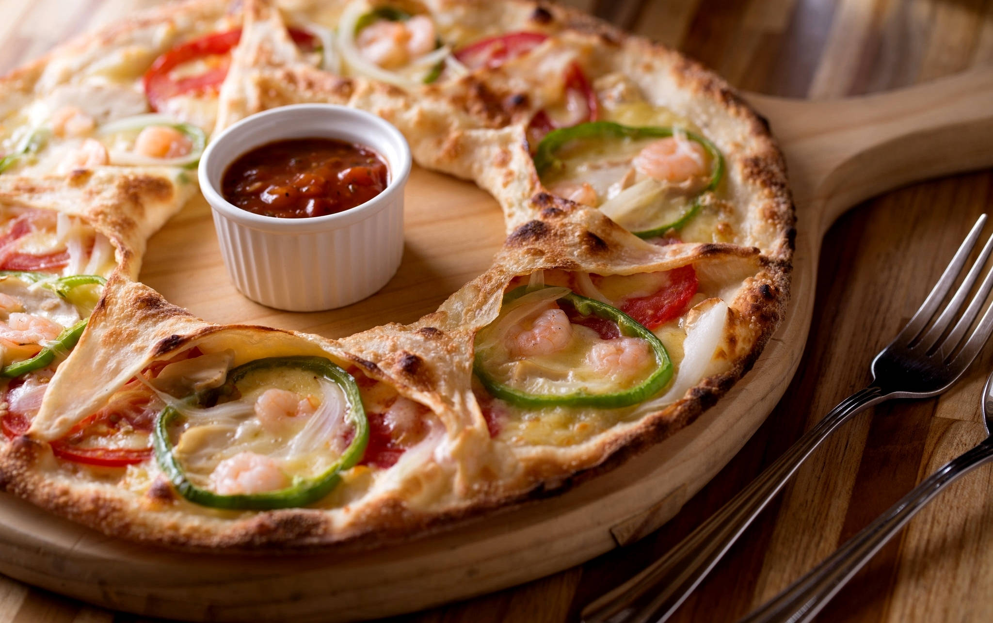 Pizza 桌布 壁紙 — 新鮮出爐的披薩，上面有蝦、青椒和番茄，放在木板上，附上沾醬和叉子。