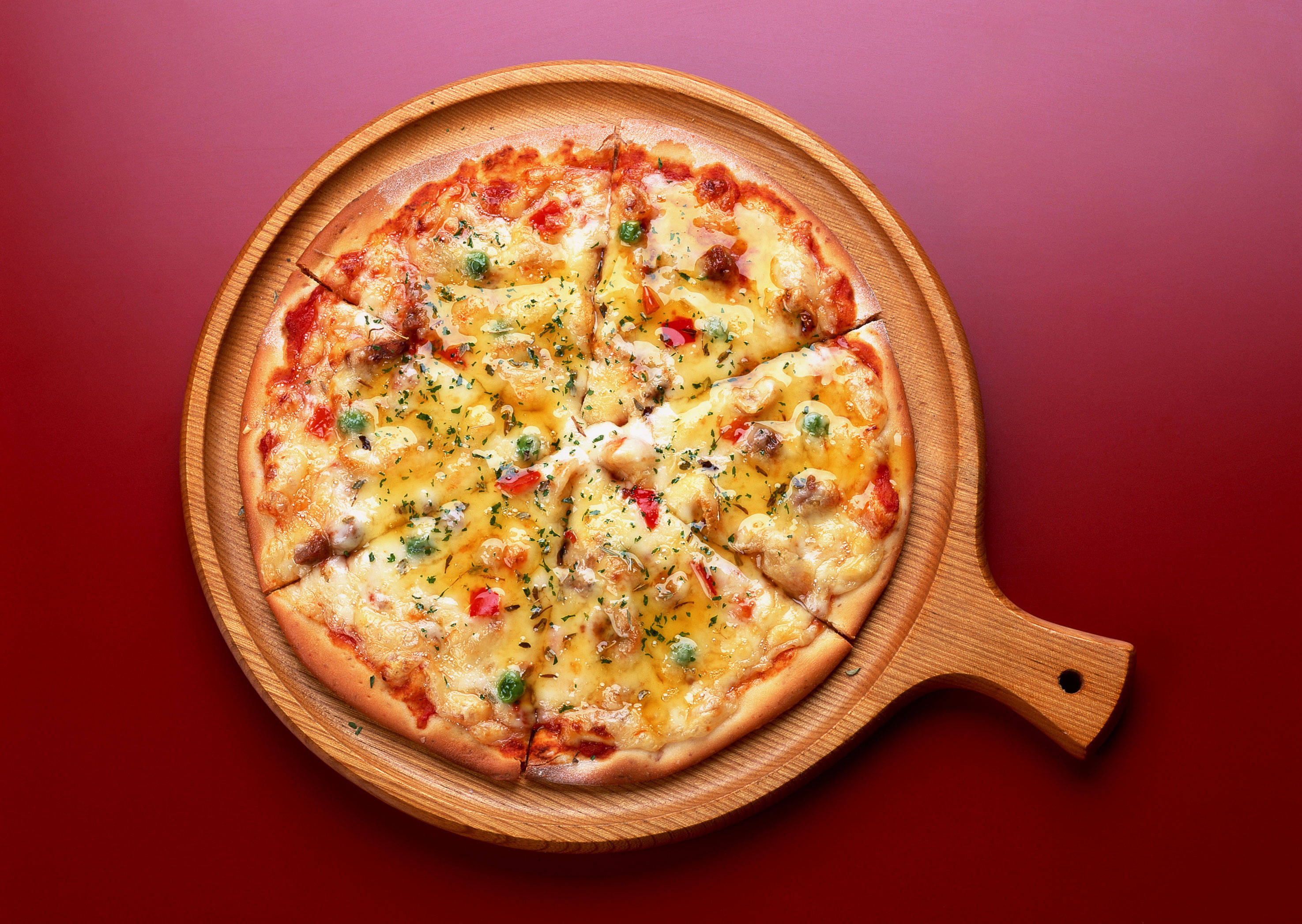 Pizza 桌布 壁紙 — 新鮮出爐的披薩，上面有融化的起司和配料，放在木製托盤上，背景為深紅色。