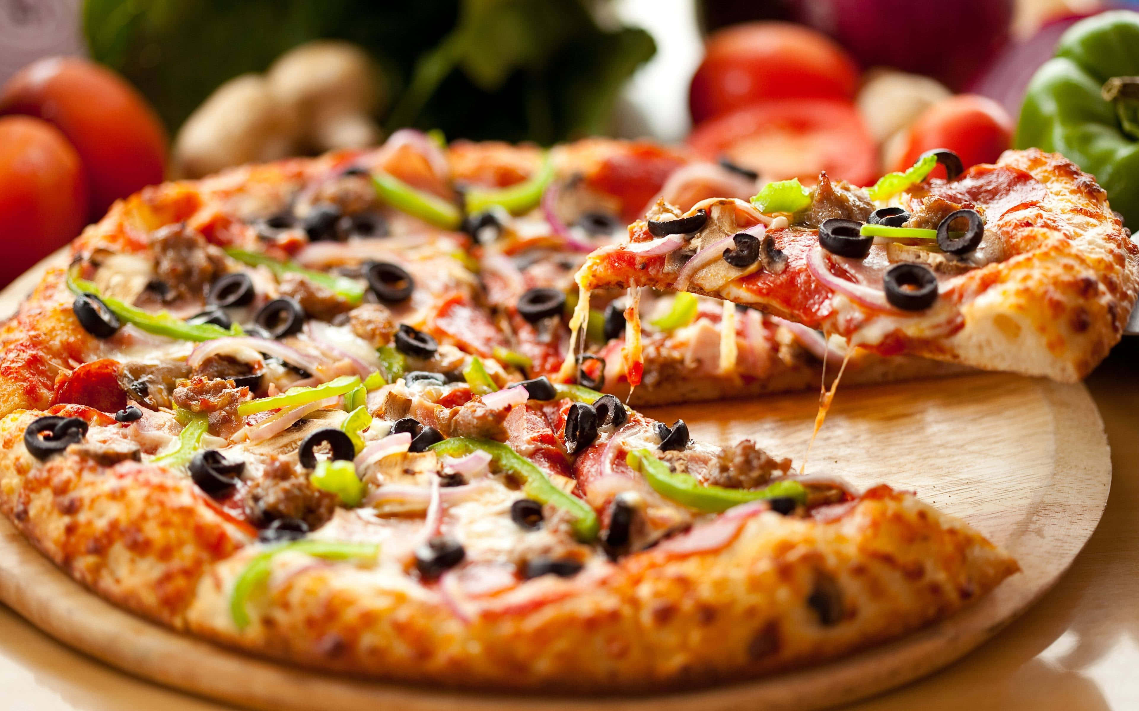 Pizza 桌布 壁紙 — 新鮮出爐的披薩，上面有融化的起司和配料，放在木板上，其中一片被拿起，露出牽絲的起司。