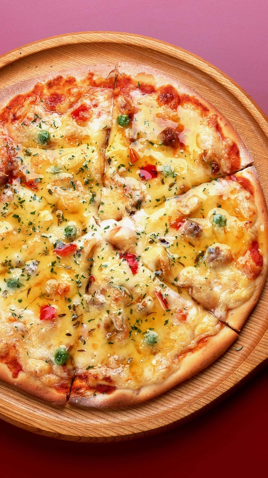 Pizza 桌布 壁紙 — 新鮮出爐的披薩，上面有融化的起司和色彩繽紛的配料，放在木製托盤上，背景是充滿活力的粉紅色和紅色。
