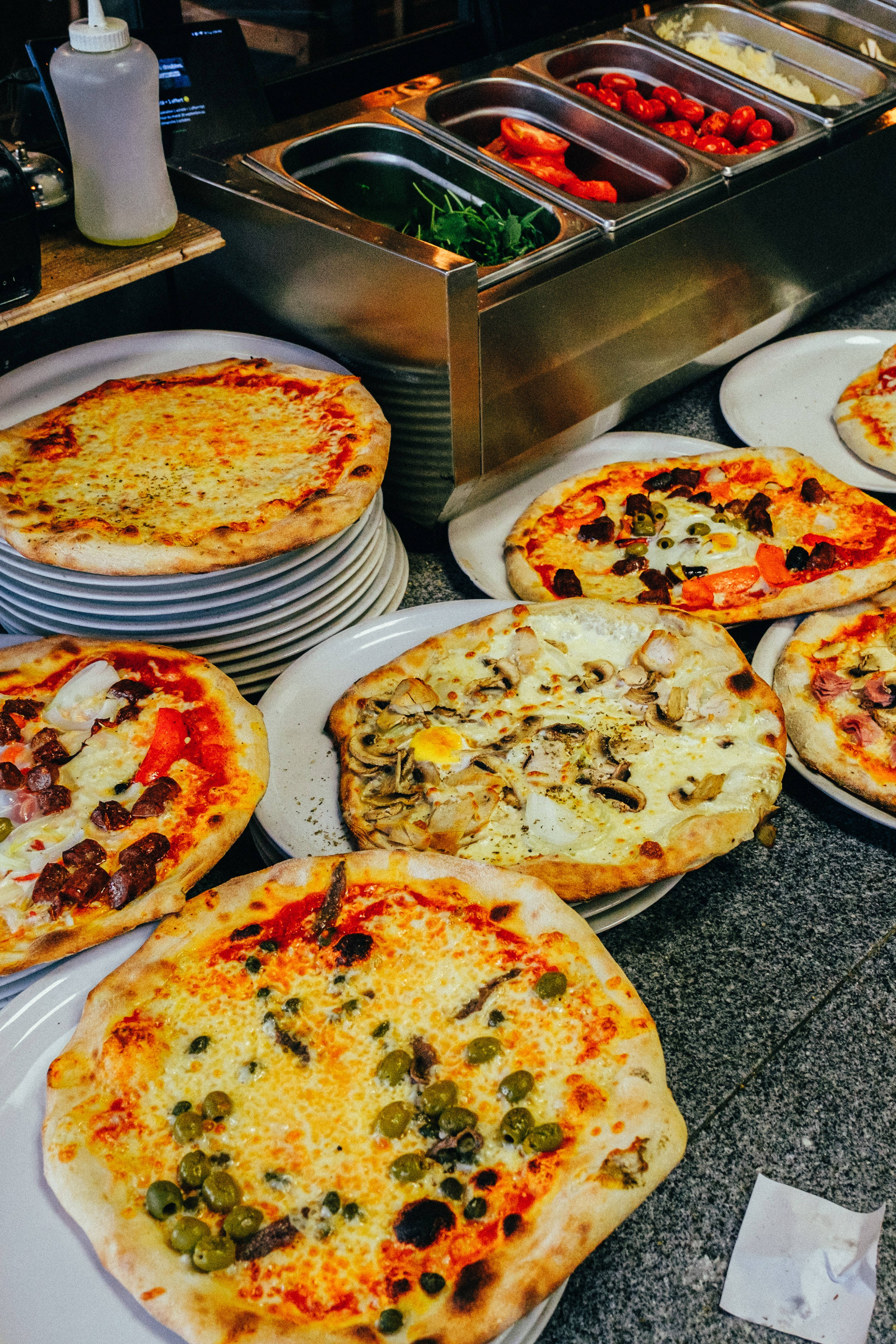 Dominos Pizza 桌布 壁紙 — 新鮮出爐的披薩，上面有酸豆、鯷魚和蘑菇等各種配料，放在盤子上，旁邊有一個不鏽鋼調味料站。