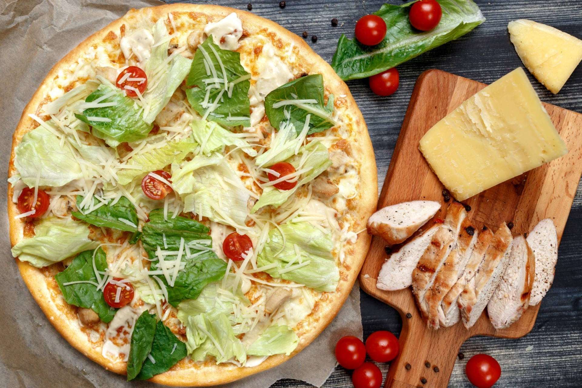 Pizza 桌布 壁紙 — 新鮮出爐的披薩，上面鋪有生菜、櫻桃番茄和起司，旁邊是烤雞和起司，放在木板上。