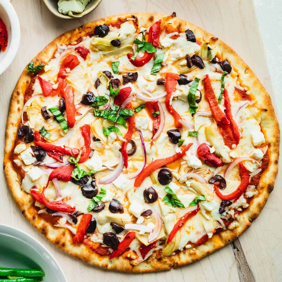 Pizza 桌布 壁紙 — 新鮮出爐的披薩，上面鋪有紅甜椒、黑橄欖、朝鮮薊和羅勒，放在淺色木質表面上。