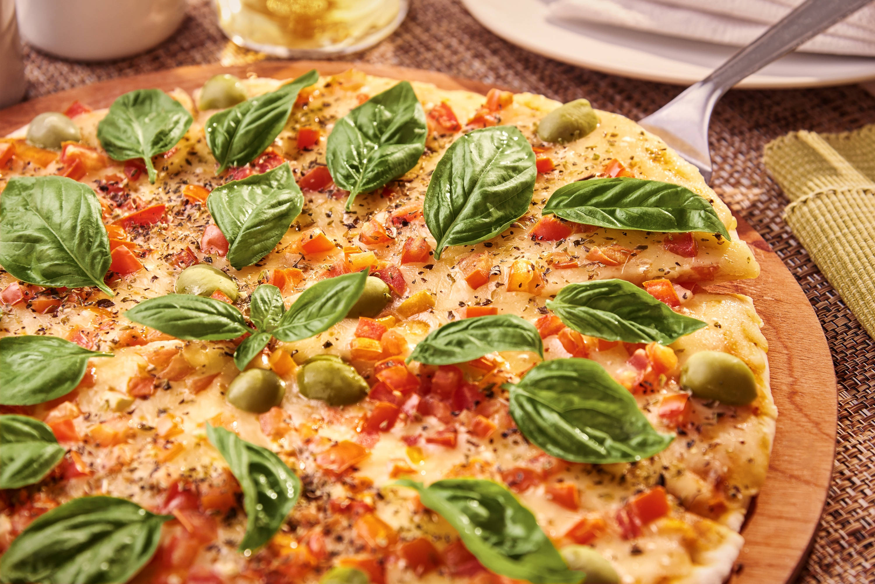 Pizza 桌布 壁紙 — 新鮮出爐的披薩，上面鋪滿羅勒、橄欖和甜椒，放在木板上準備上桌。