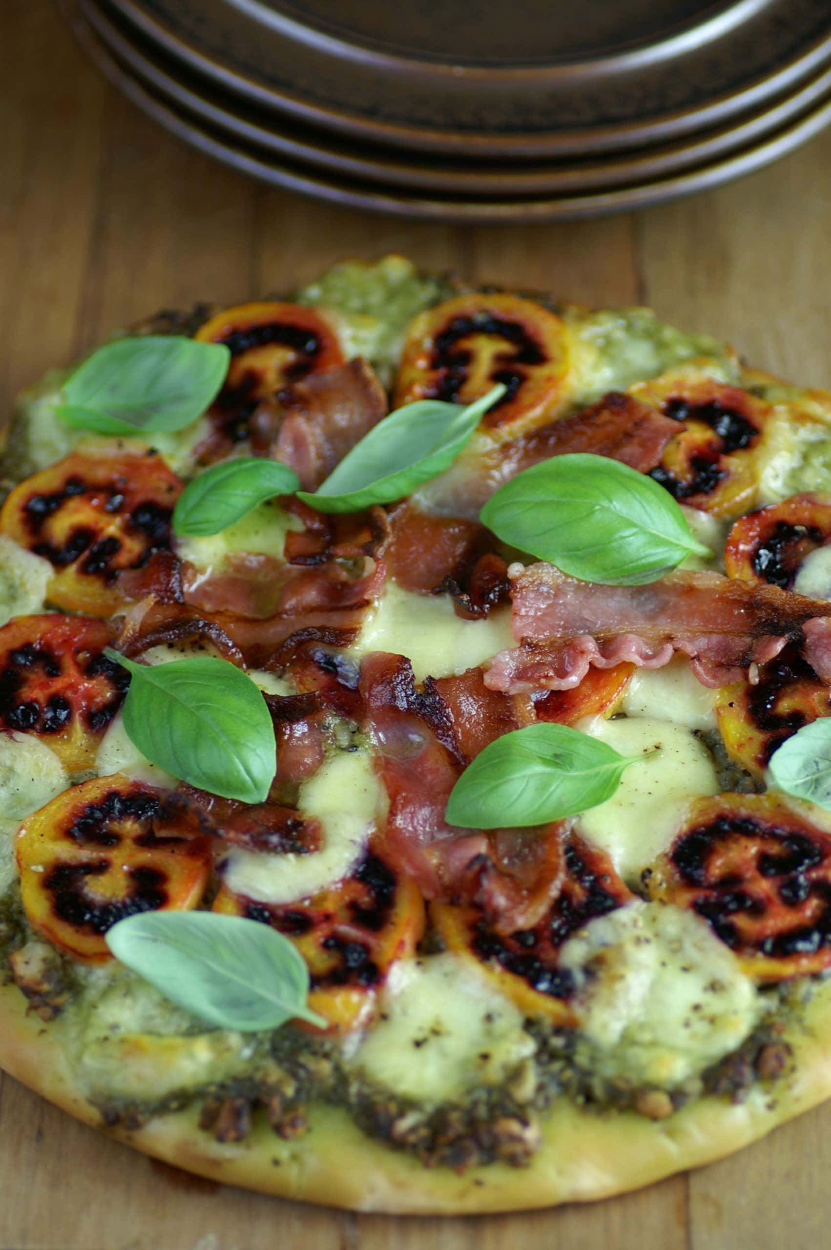 Pizza 桌布 壁紙 — 新鮮出爐的披薩上面鋪了烤番茄、羅勒和脆培根，放在木板上，附近有疊起的盤子。