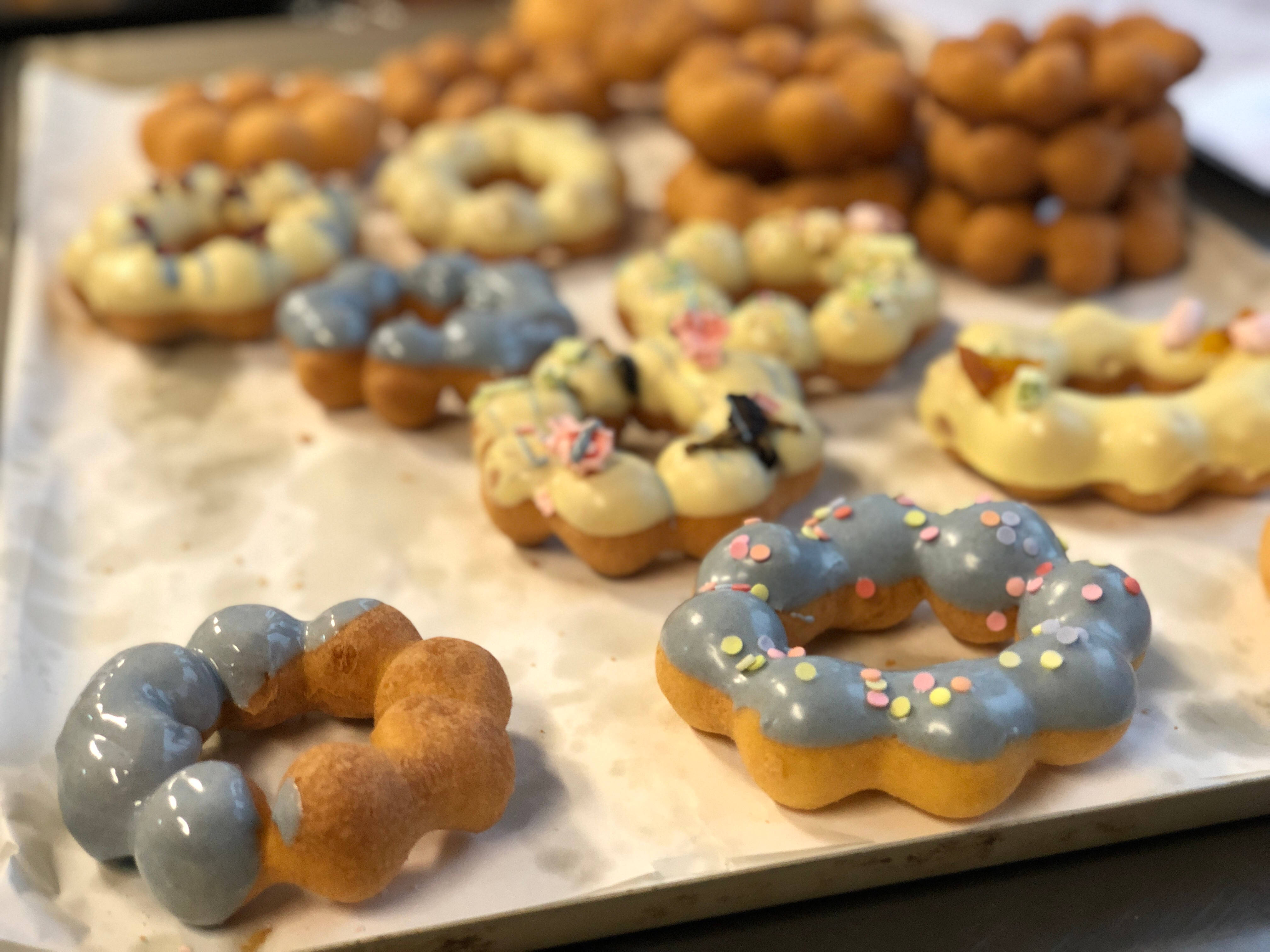 Donut 桌布 壁紙 — 新鮮出爐的泡泡甜甜圈，配上藍色和黃色糖霜及彩色糖粒，放在鋪有烘焙紙的烤盤上。