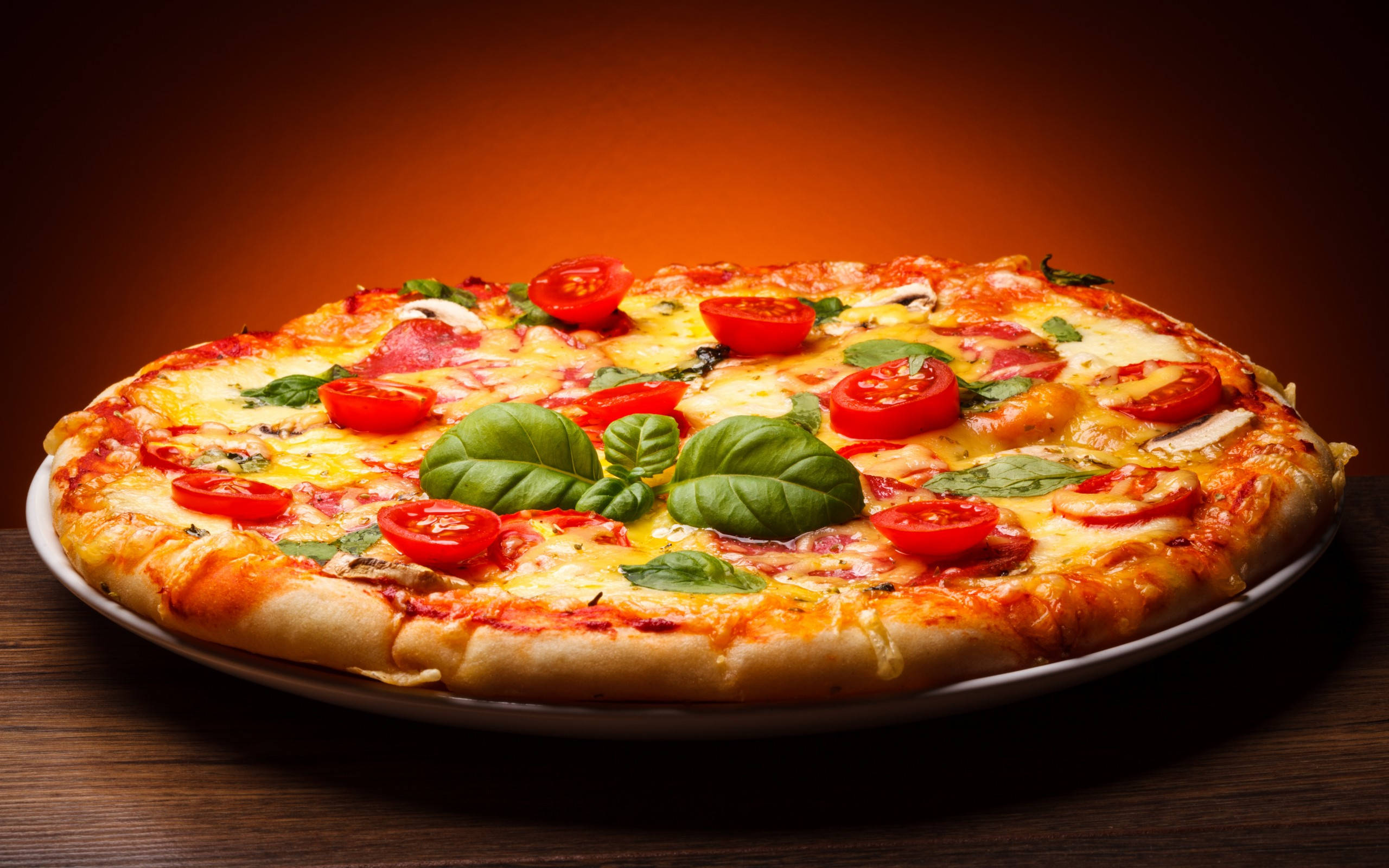 Pizza 桌布 壁紙 — 新鮮出爐的瑪格麗特披薩，上面有融化的起司、番茄片和羅勒葉，放在木桌上，在溫暖的燈光下。
