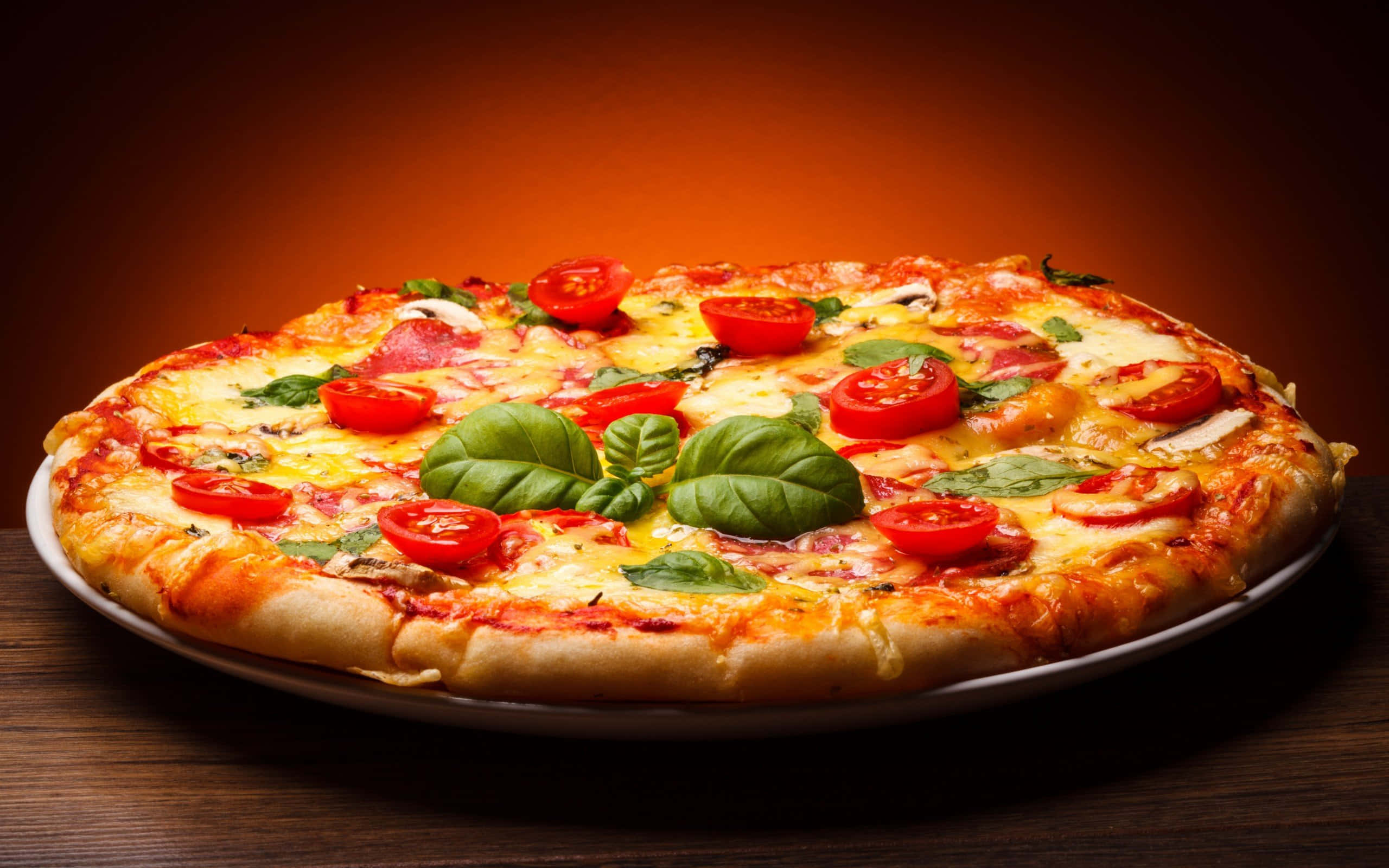 Pizza 桌布 壁紙 — 新鮮出爐的瑪格麗特披薩，上面有融化的起司、番茄片和羅勒葉，放在木桌上，在溫暖的燈光下。