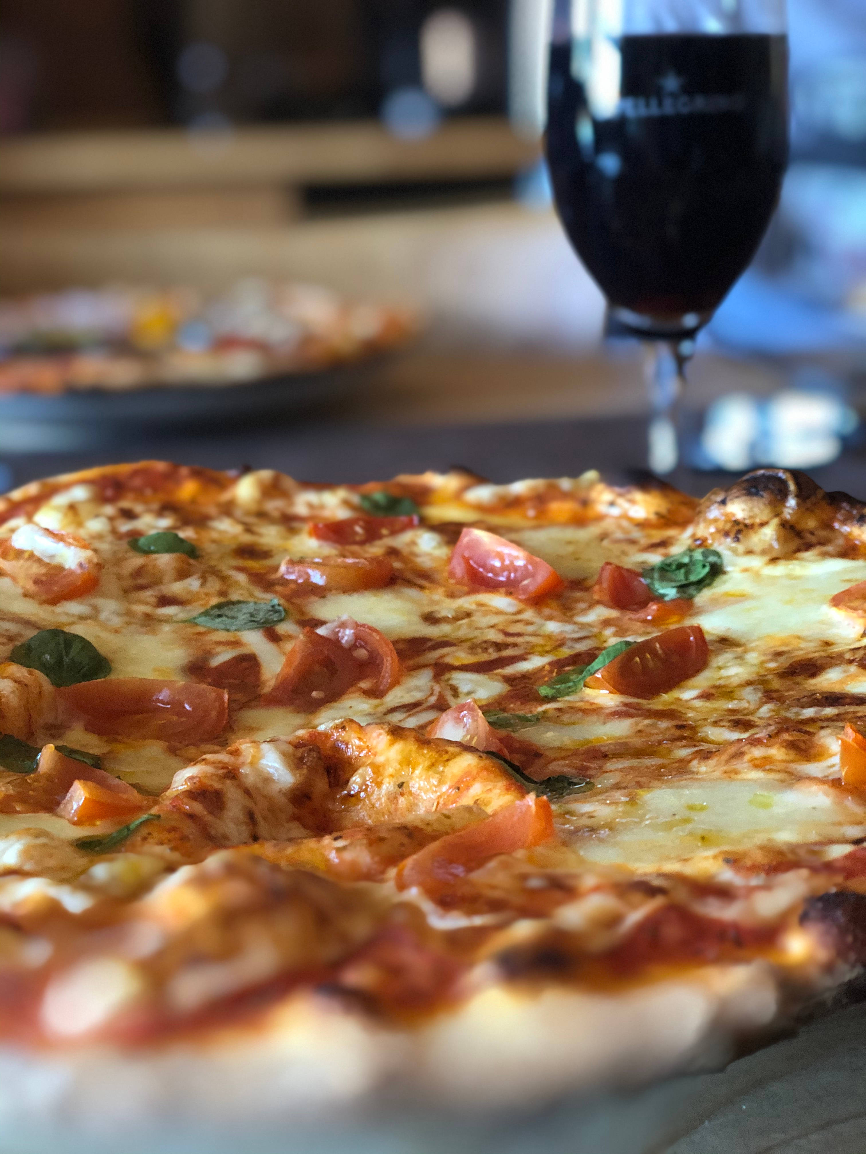 Pizza 桌布 壁紙 — 新鮮出爐的瑪格麗特披薩特寫，配以融化起司、番茄片和羅勒葉，旁邊放著一杯黑啤酒。