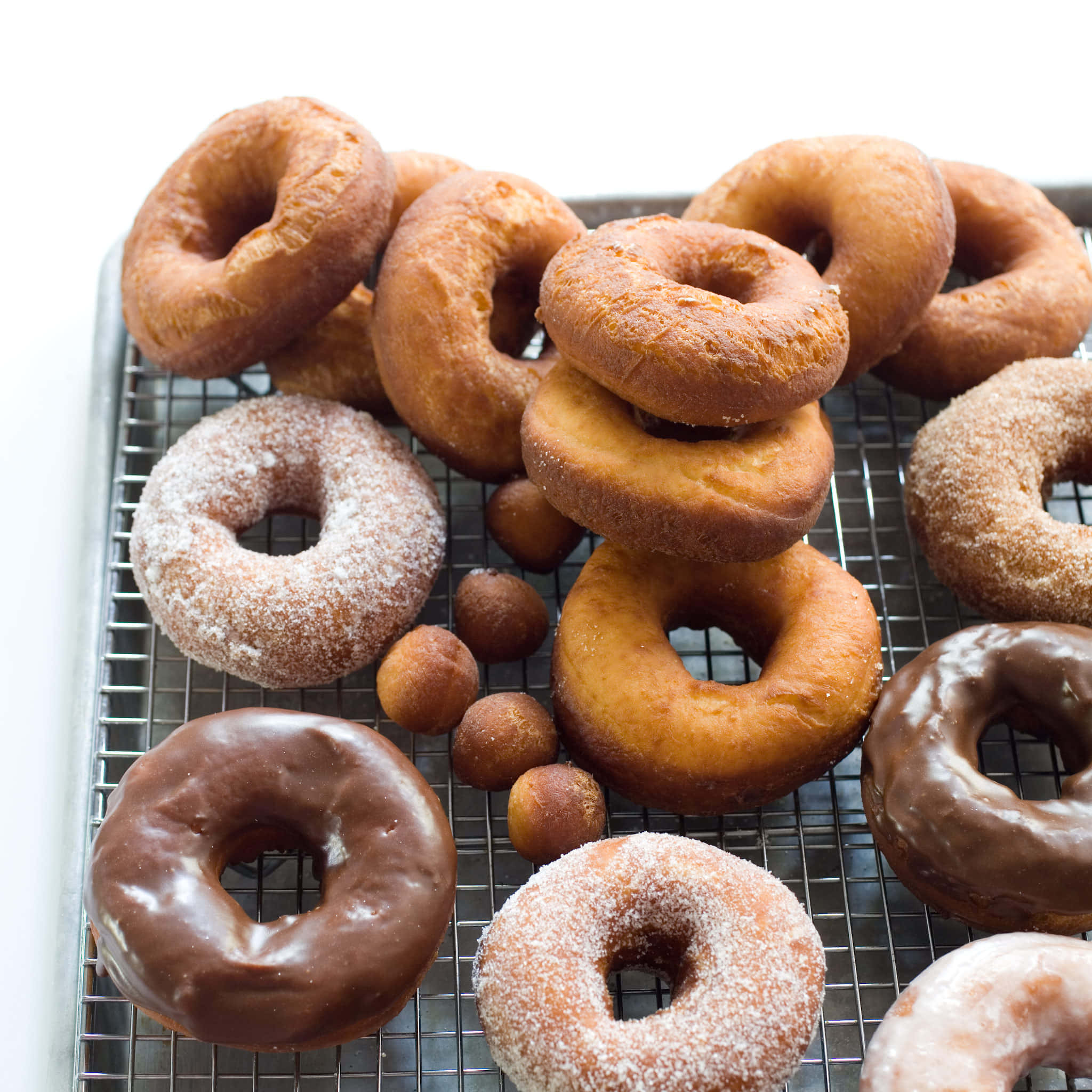 Glazed Donut 桌布 壁紙 — 新鮮出爐的甜甜圈，配上巧克力糖霜、糖衣和肉桂糖，堆放在冷卻架上。