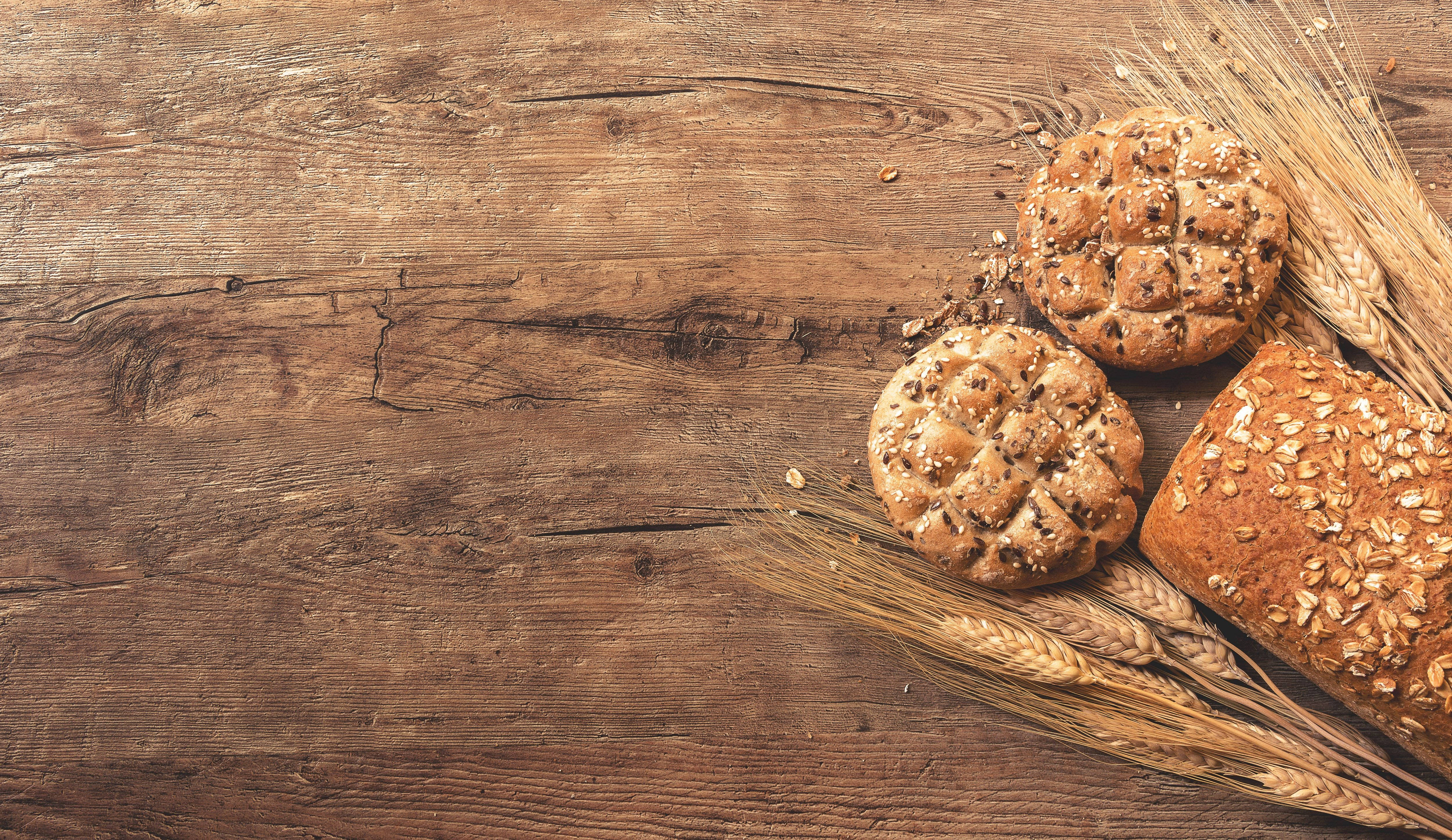Bakery 桌布 壁紙 — 新鮮出爐的種子麵包和麵包卷放在鄉村風格的木桌上，旁邊是金色的麥稈。