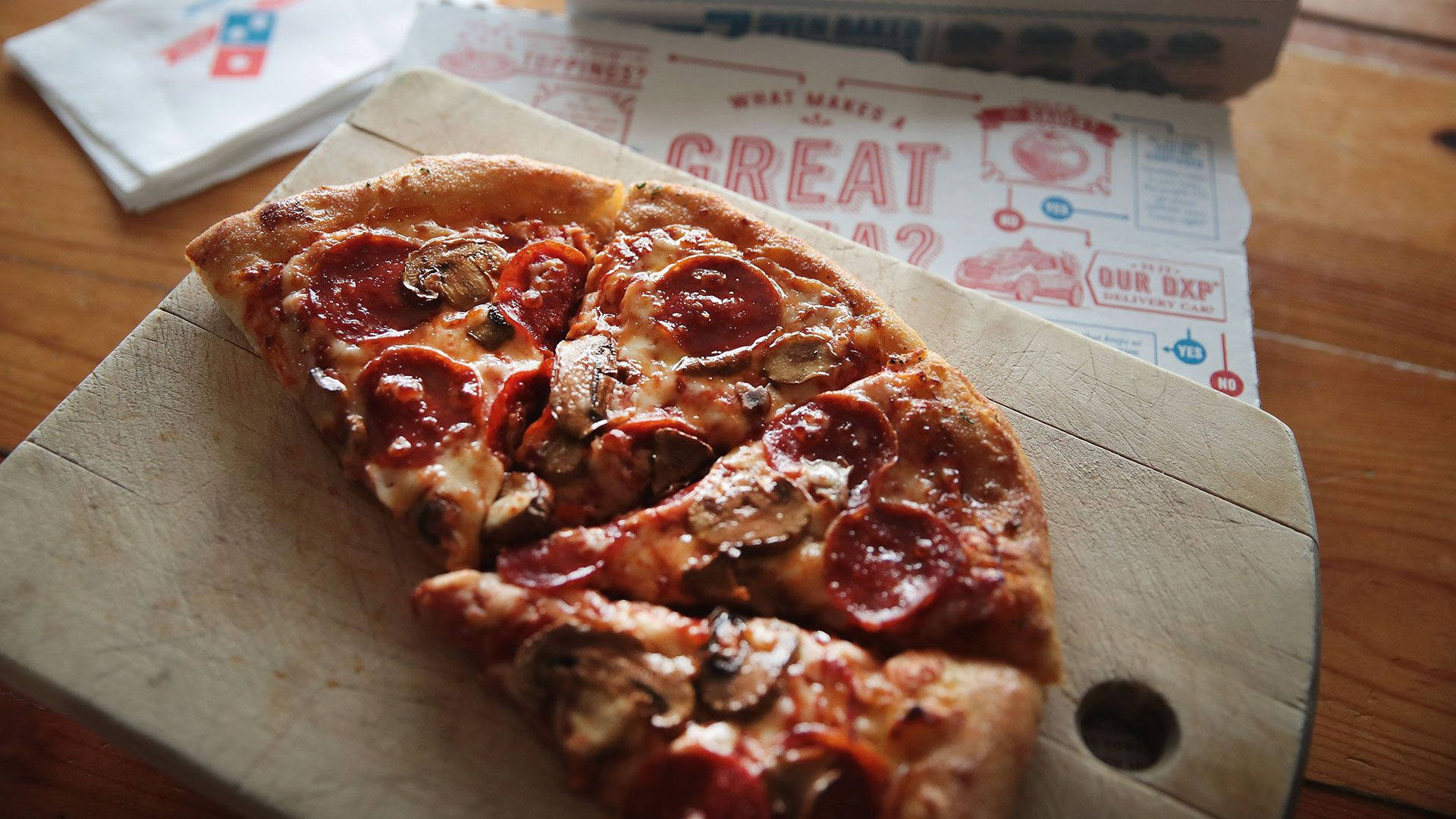 Dominos Pizza 桌布 壁紙 — 新鮮出爐的義大利辣肉腸蘑菇披薩放在一個木製砧板上，砧板下方是一張鄉村風格的木桌。