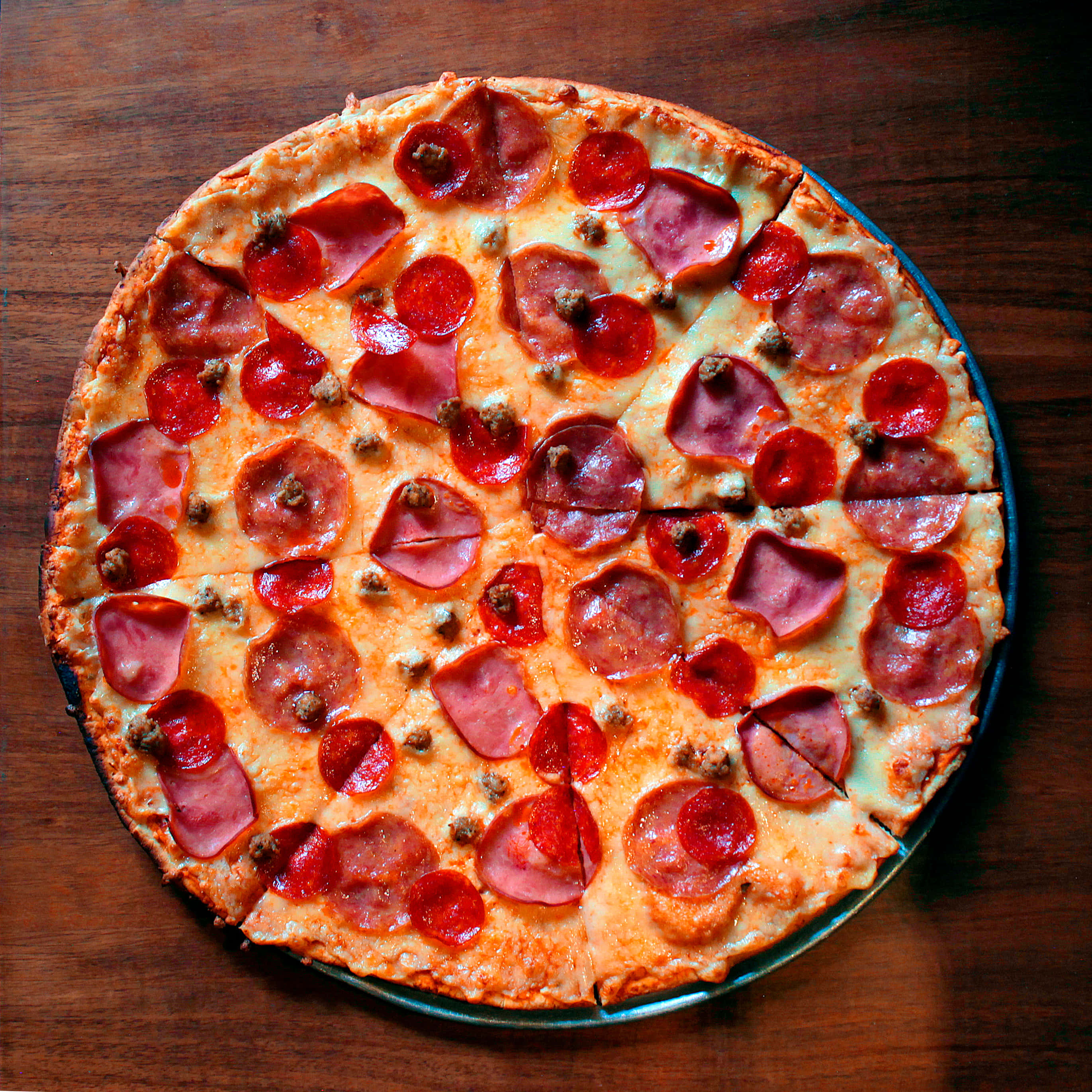 Pizza 桌布 壁紙 — 新鮮出爐的義大利辣香腸和香腸披薩，配上融化的起司，切片放在深色木桌上。