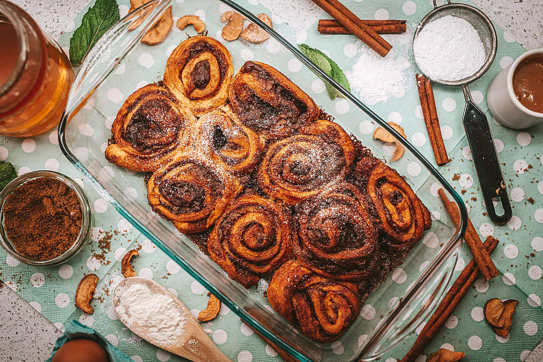 Pastries 桌布 壁紙 — 新鮮出爐的肉桂捲放在玻璃盤中，周圍是香料和食材，置於圓點布上。