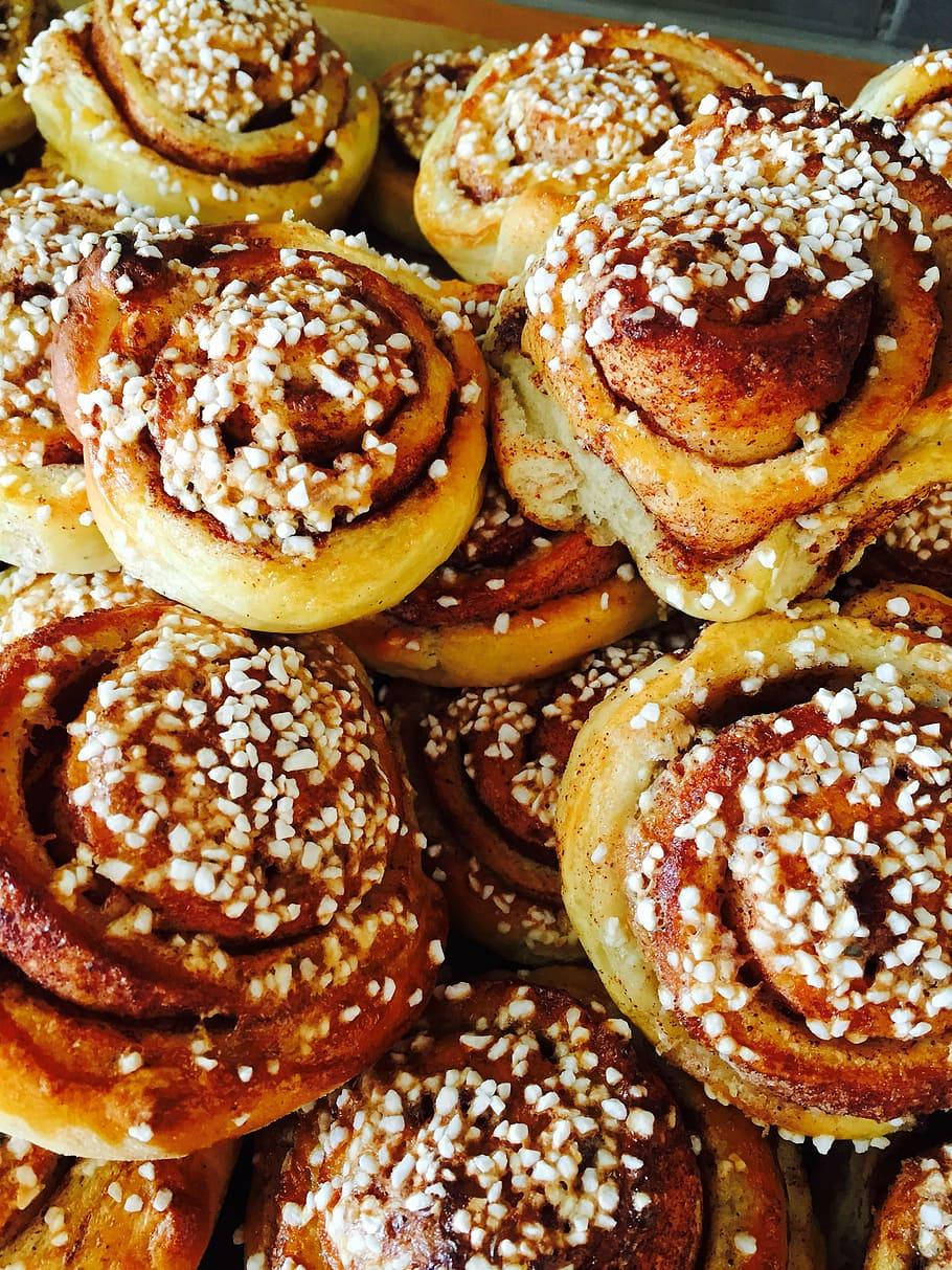 Pastry 桌布 壁紙 — 新鮮出爐的肉桂捲高高堆起，金黃色的漩渦和白色糖晶在溫暖燈光下閃閃發光。