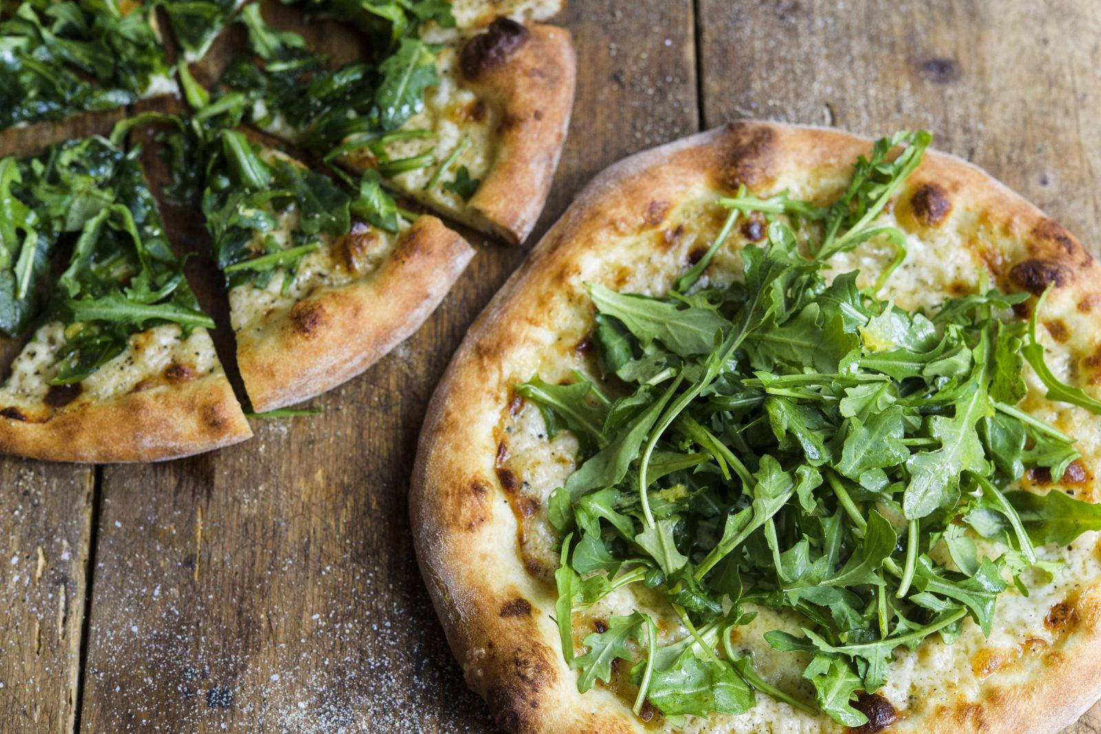 Pizza 桌布 壁紙 — 新鮮出爐的芝麻葉披薩，金黃色的餅皮切片放在鄉村風格的木桌上。