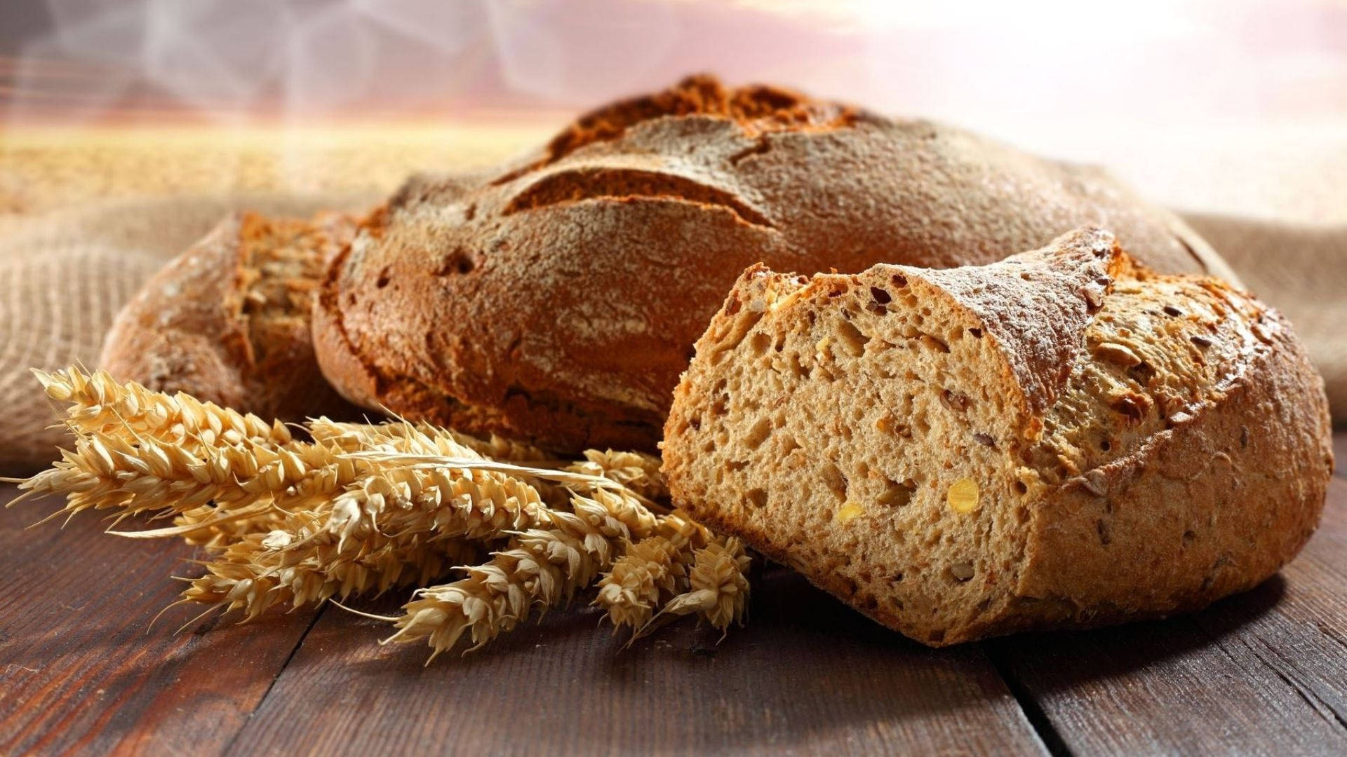 Bread 桌布 壁紙 — 新鮮出爐的鄉村麵包，金黃酥脆的外皮，搭配麥穗，放在深色木桌上。