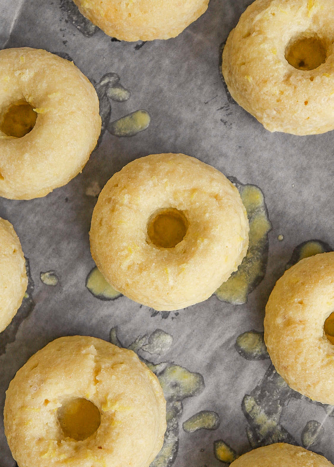 Glazed Donut 桌布 壁紙 — 新鮮出爐的金色甜甜圈，上面有融化的奶油池，放在鋪了油膩烘焙紙的烤盤上。