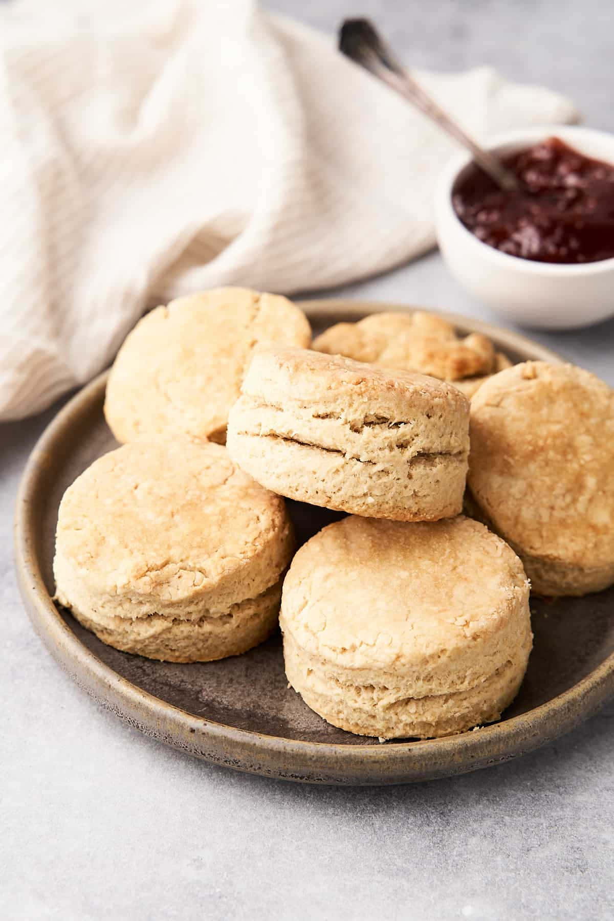 Biscuit 桌布 壁紙 — 新鮮出爐的金黃色餅乾堆疊在一個鄉村風格的盤子上，旁邊是一小碗深紅色果醬和一條奶油色的布餐巾。
