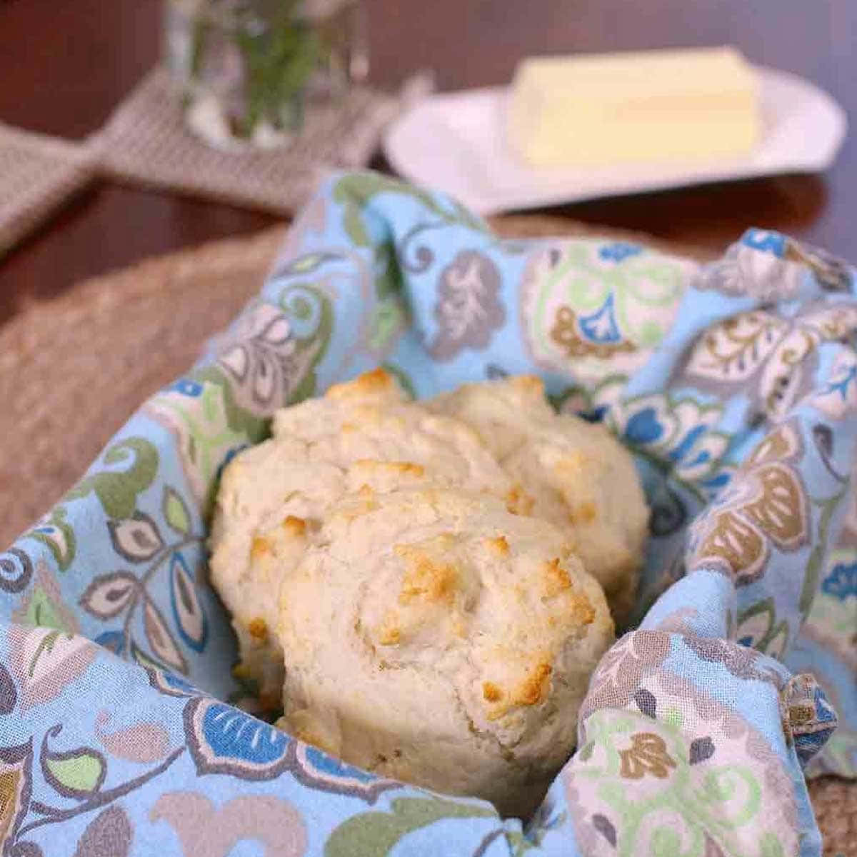 Biscuit 桌布 壁紙 — 新鮮出爐的金黃色餅乾放在有圖案的藍色布餐巾上，旁邊有奶油，置於木桌上。