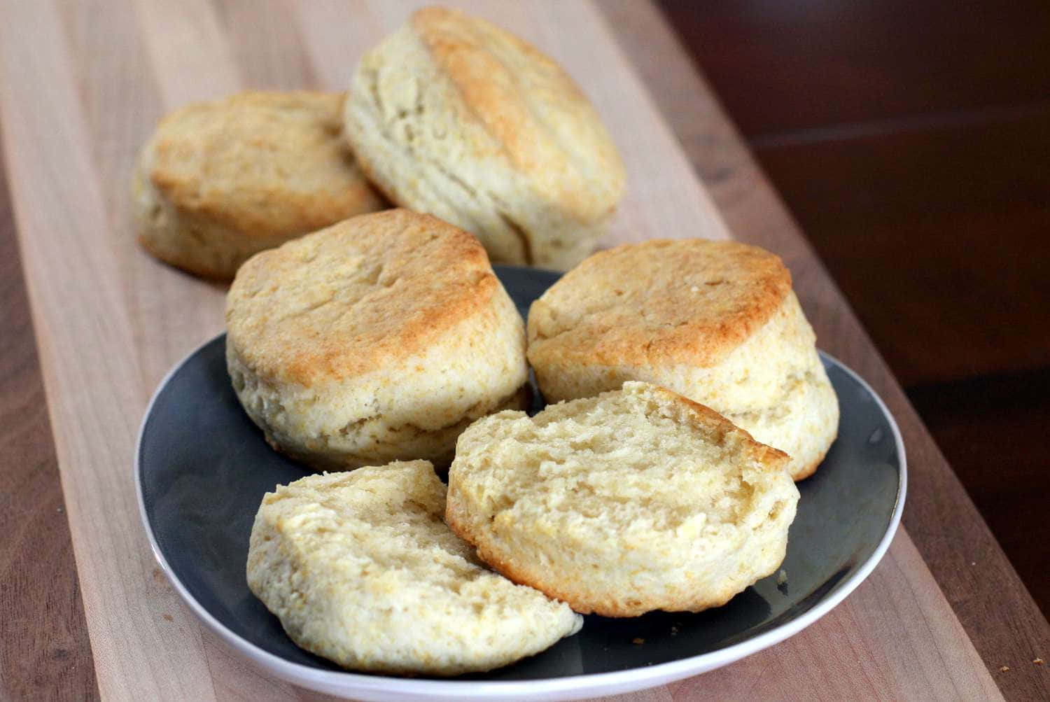 Biscuit 桌布 壁紙 — 新鮮出爐的金黃色餅乾放在木板上的一個深色盤子中，其中一塊掰開，露出柔軟蓬鬆的內部。