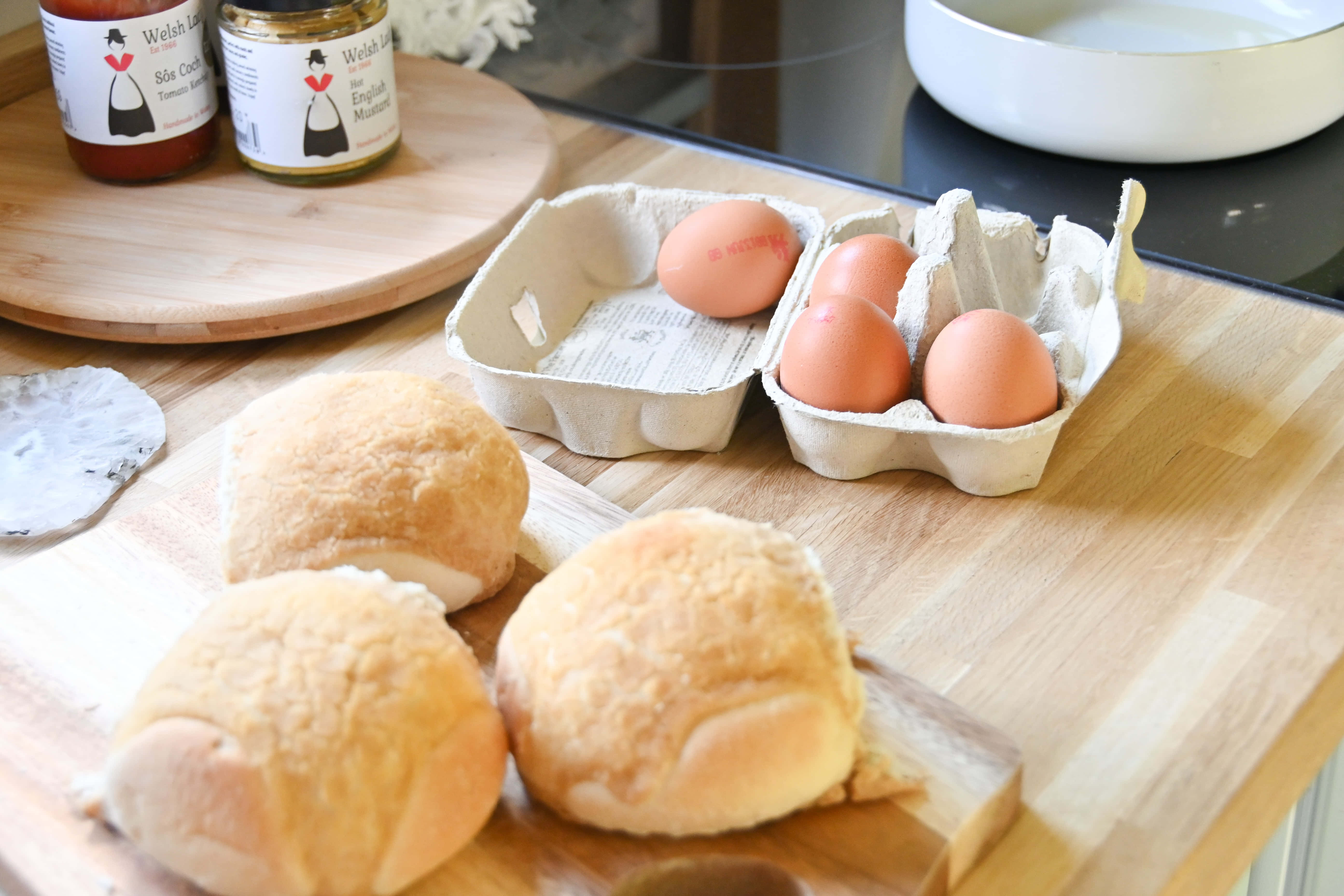 Brown Eggs 桌布 壁紙 — 新鮮出爐的金黃色麵包卷和棕色雞蛋放在木製檯面上，旁邊是威爾斯調味醬罐。