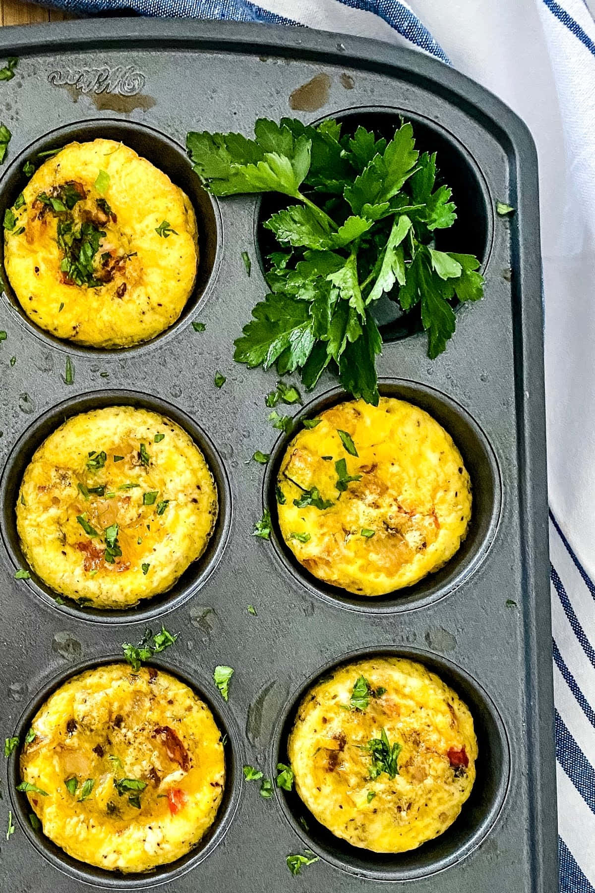 Scrambled Egg 桌布 壁紙 — 新鮮出爐的雞蛋馬芬放在深色金屬烤盤中，飾以巴西里，置於條紋布上。
