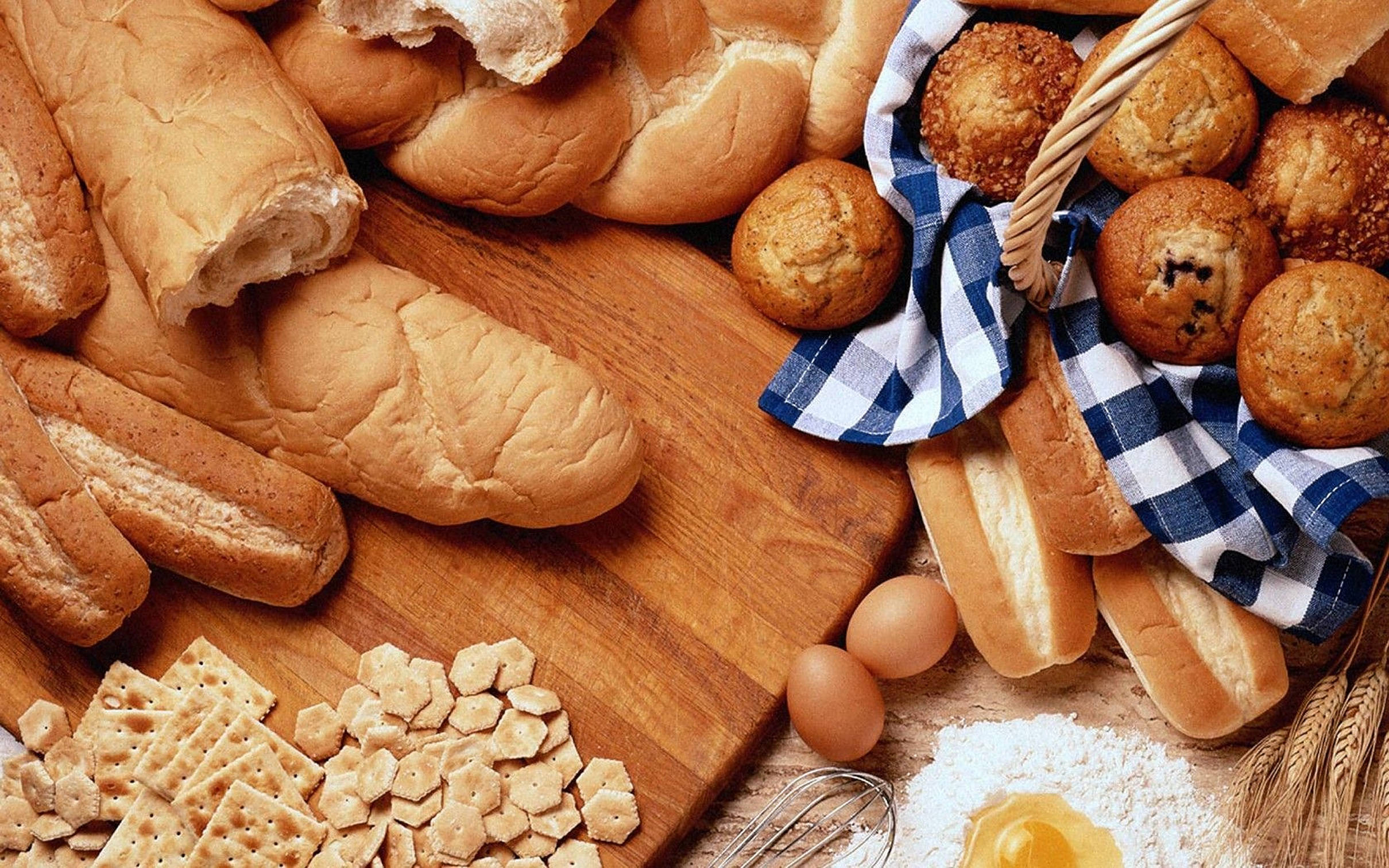 Bakery 桌布 壁紙 — 新鮮出爐的麵包卷和法式長棍麵包放在木板上，旁邊有雞蛋、麵粉、餅乾和小麥莖。