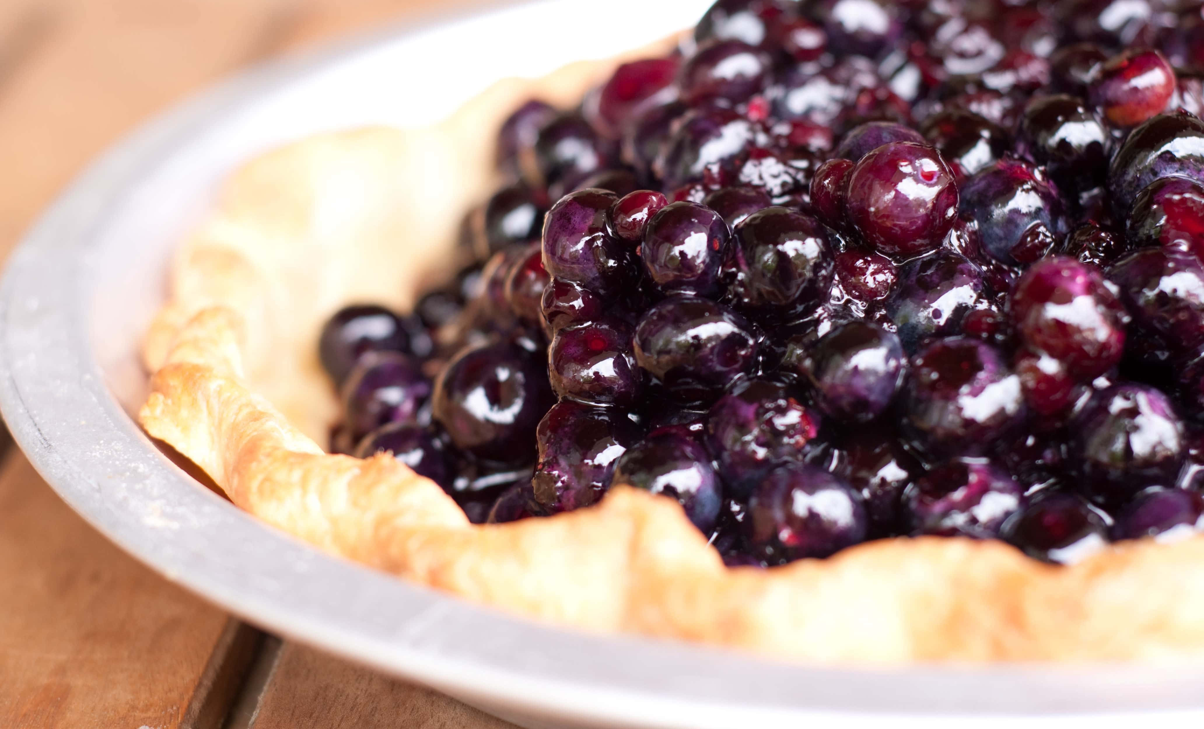 Blueberry Pie 桌布 壁紙 — 新鮮出爐藍莓派的特寫，閃亮的莓果從金屬盤中的金黃色外皮溢出。