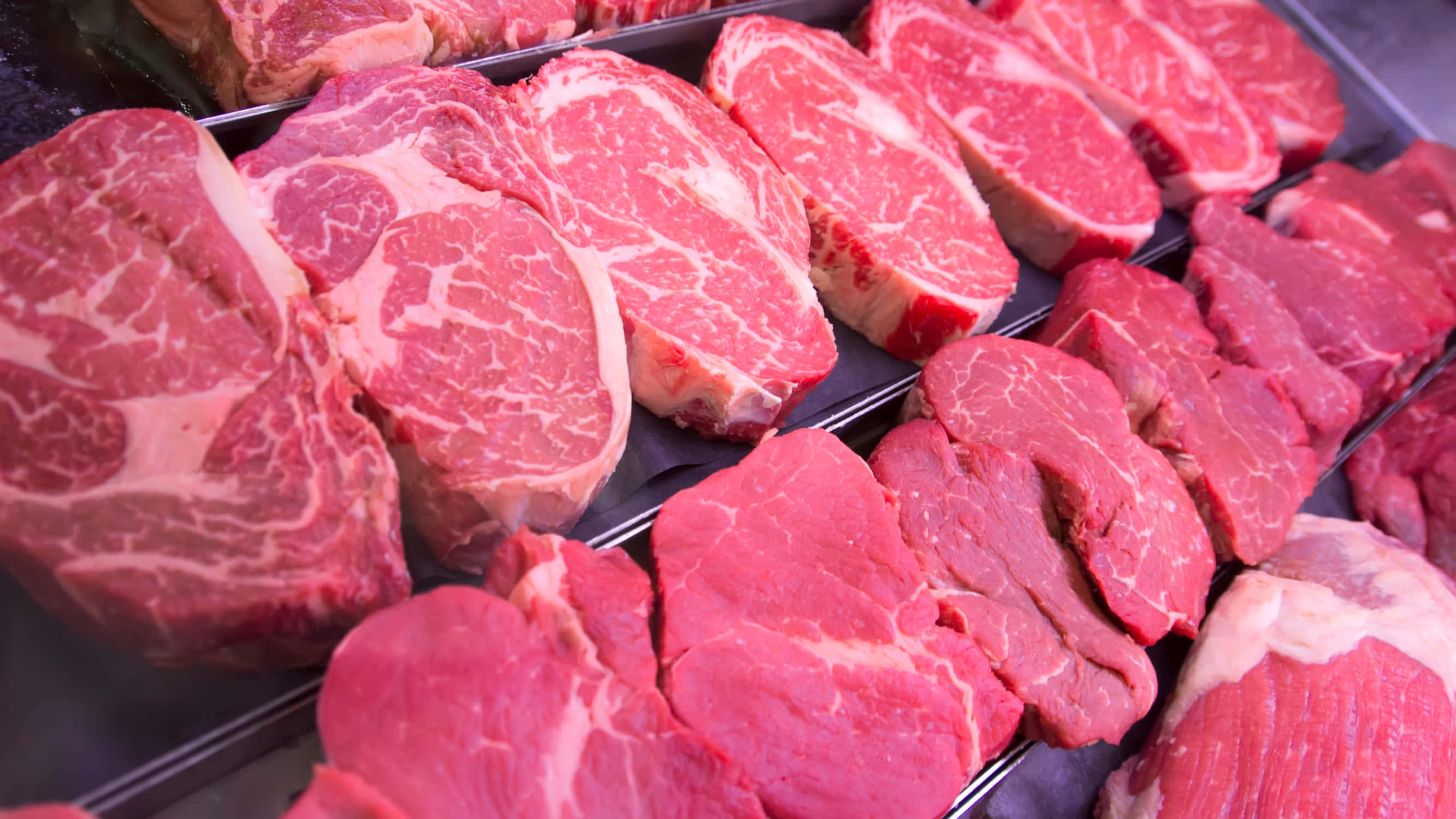 meat 桌布 壁紙 — 新鮮切割的頂級牛肉牛排，帶有油花，展示在冷藏超市陳列櫃中。