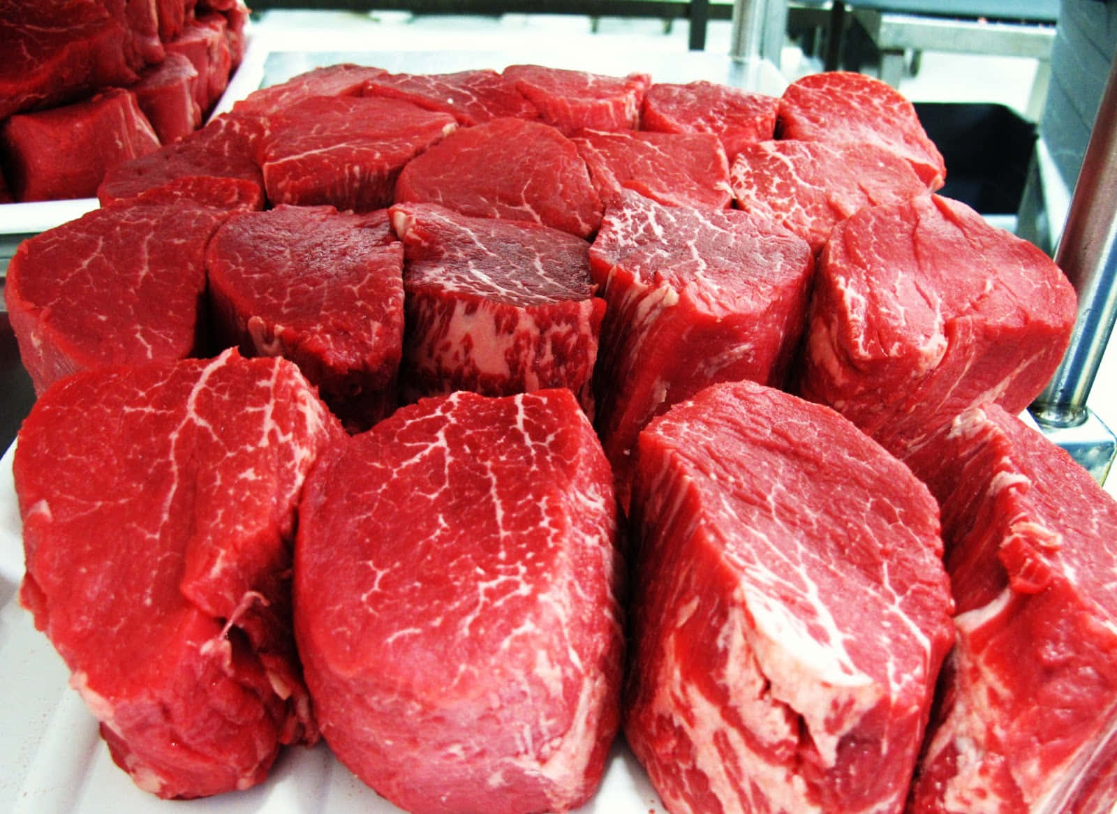 meat 桌布 壁紙 — 新鮮切好的牛肉排，呈現豐富的紅色和白色大理石花紋，放在白色托盤上，在市場環境中展示。