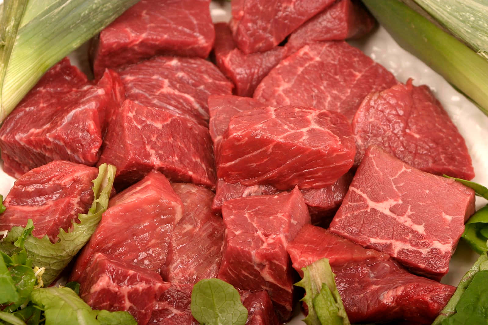 meat 桌布 壁紙 — 新鮮切好的紅色牛肉塊，帶有白色大理石紋，被綠色韭蔥和生菜圍繞，放在白色盤子上。