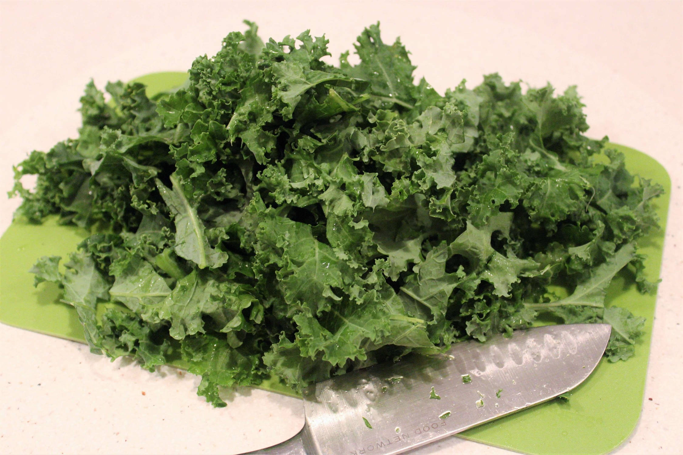 Cabbage 桌布 壁紙 — 新鮮切好的羽衣甘藍高高堆在綠色砧板上，旁邊放著一把廚師刀。