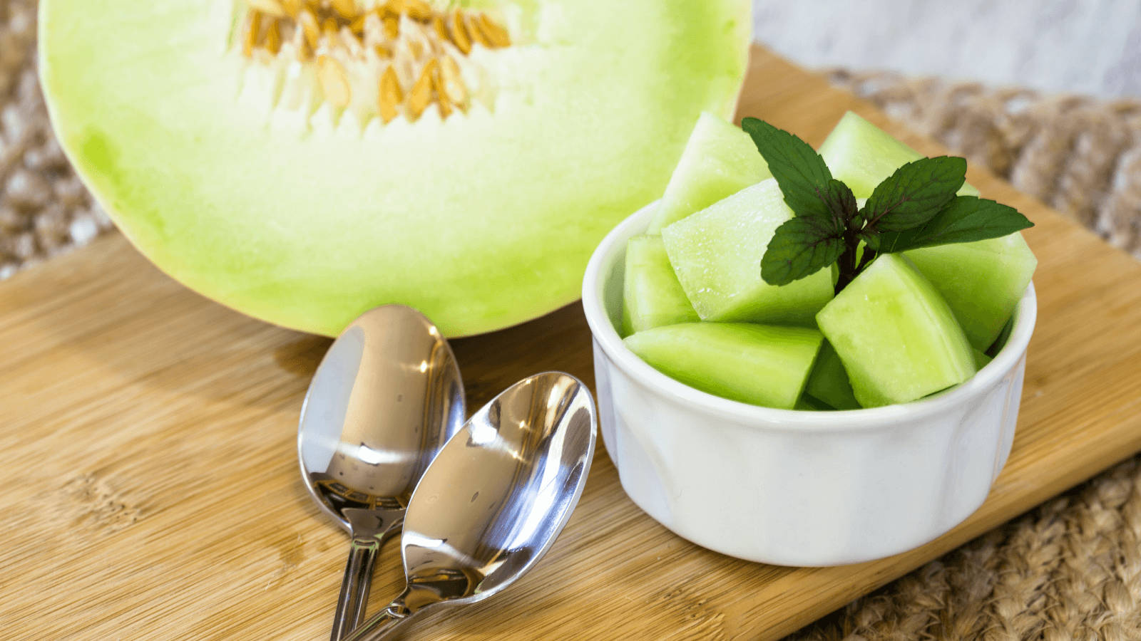 Fruits 桌布 壁紙 — 新鮮切好的蜜瓜塊放在白色碗中，配上薄荷裝飾，旁邊是半個蜜瓜放在木板上。
