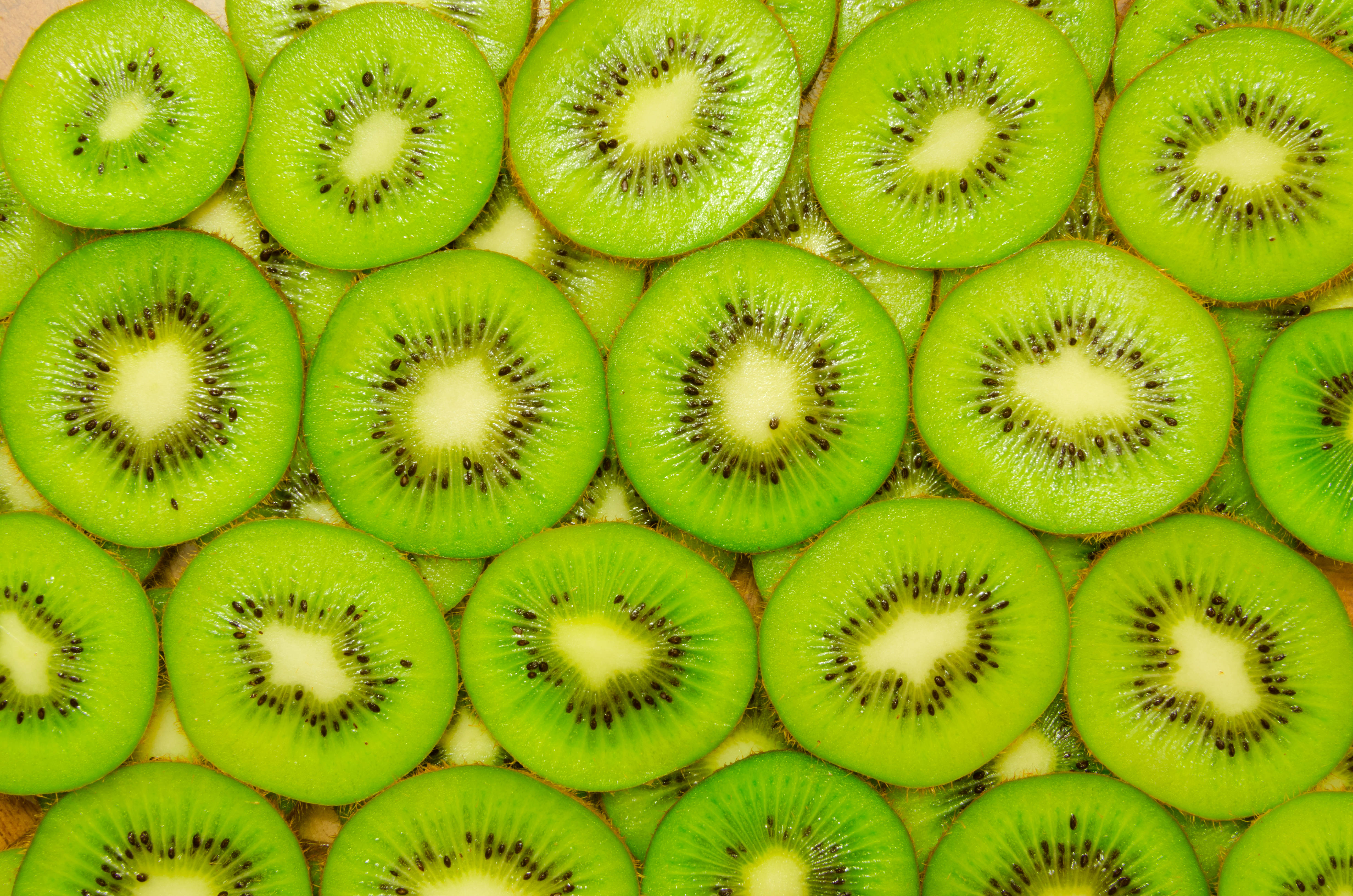 Fruits 桌布 壁紙 — 新鮮切片奇異果以密集重疊圖案排列的鮮豔特寫，展現多汁的綠色果肉和黑色種子。