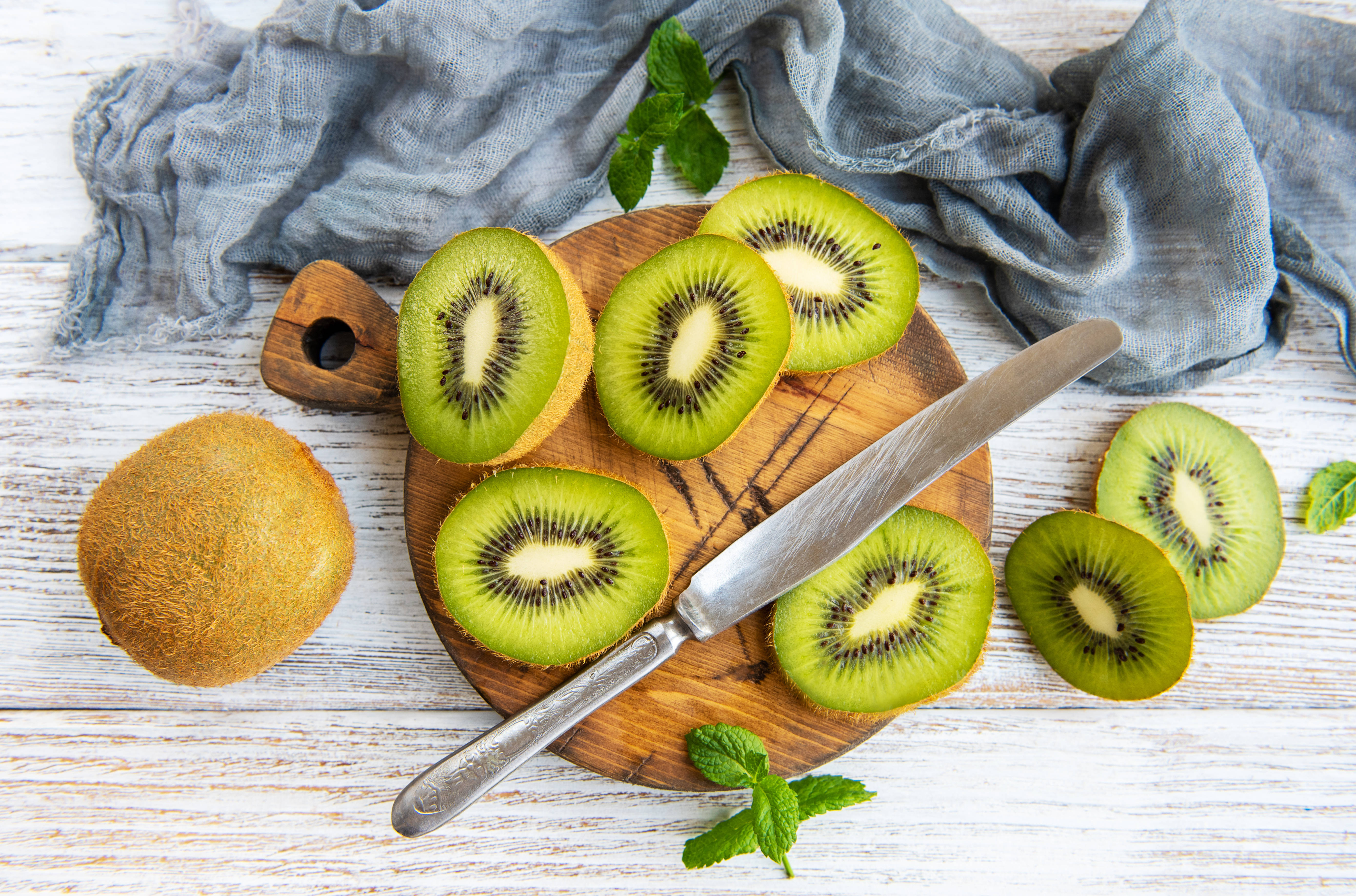 Kiwi 桌布 壁紙 — 新鮮切片奇異果搭配薄荷葉和一把刀，放在質樸的木板上，背景是風化的白色木頭。