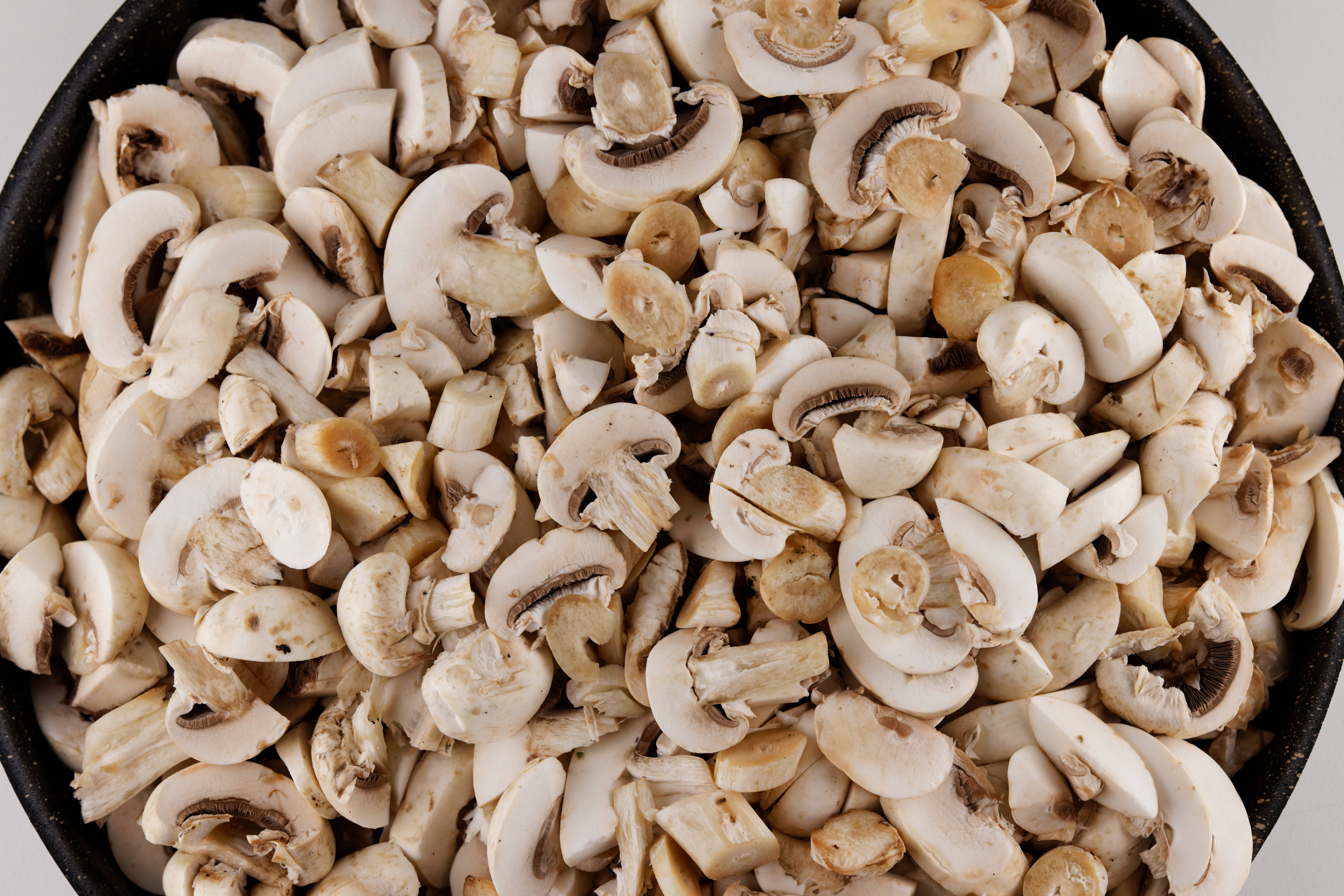 Mushroom 桌布 壁紙 — 新鮮切片白蘑菇的特寫，填滿黑色煎鍋，展示其奶油色菌蓋和泥土色菌褶。