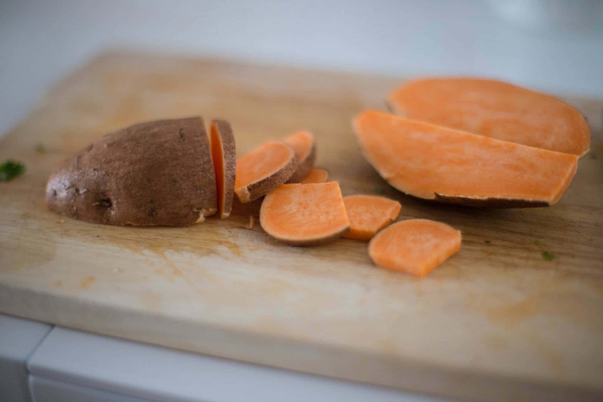 Yellow Sweet Potato 桌布 壁紙 — 新鮮切片的番薯，帶有鮮豔橙色的果肉，放在木製砧板上。