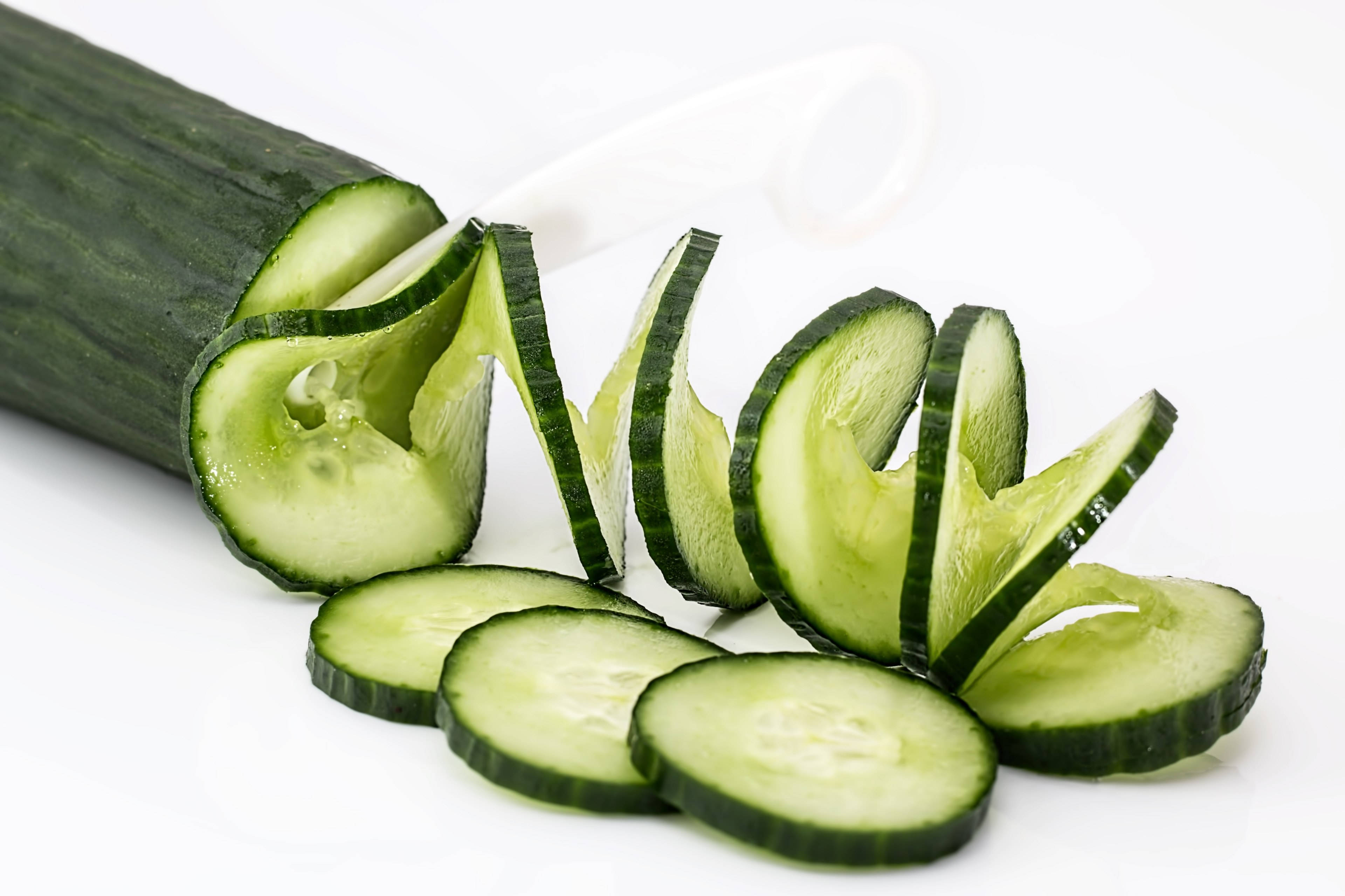 Vegetable 桌布 壁紙 — 新鮮切片的綠色黃瓜片藝術性地排列在明亮的白色背景上，附近有一條完整的黃瓜和刀。