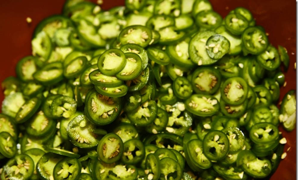 Spicy 桌布 壁紙 — 新鮮切片青墨西哥辣椒堆放在微紅色碗中的特寫，露出種子和鮮綠色果肉。