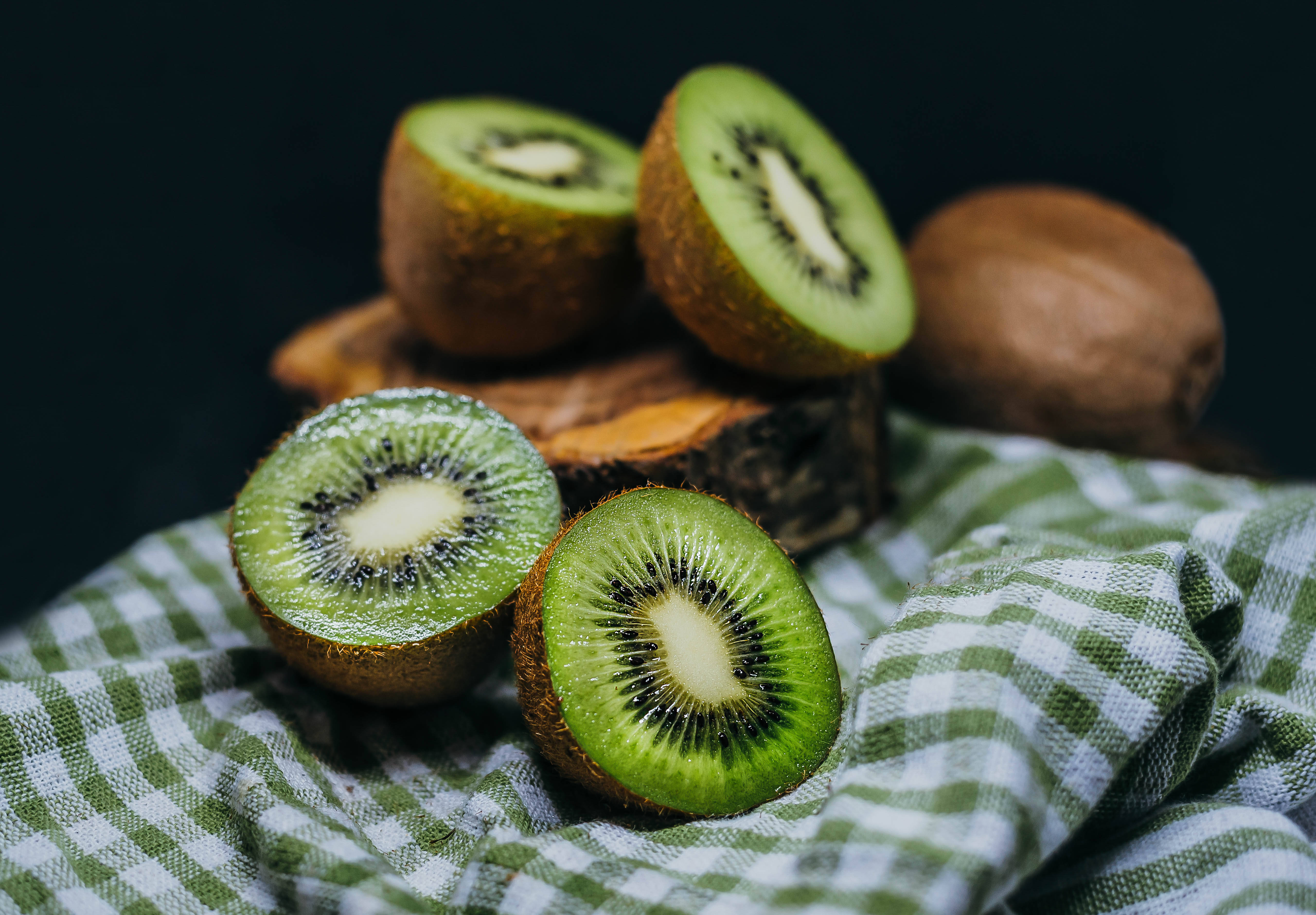 Kiwi 桌布 壁紙 — 新鮮切開的奇異果露出鮮綠色果肉和黑色種子，放在綠色和白色格子布上。