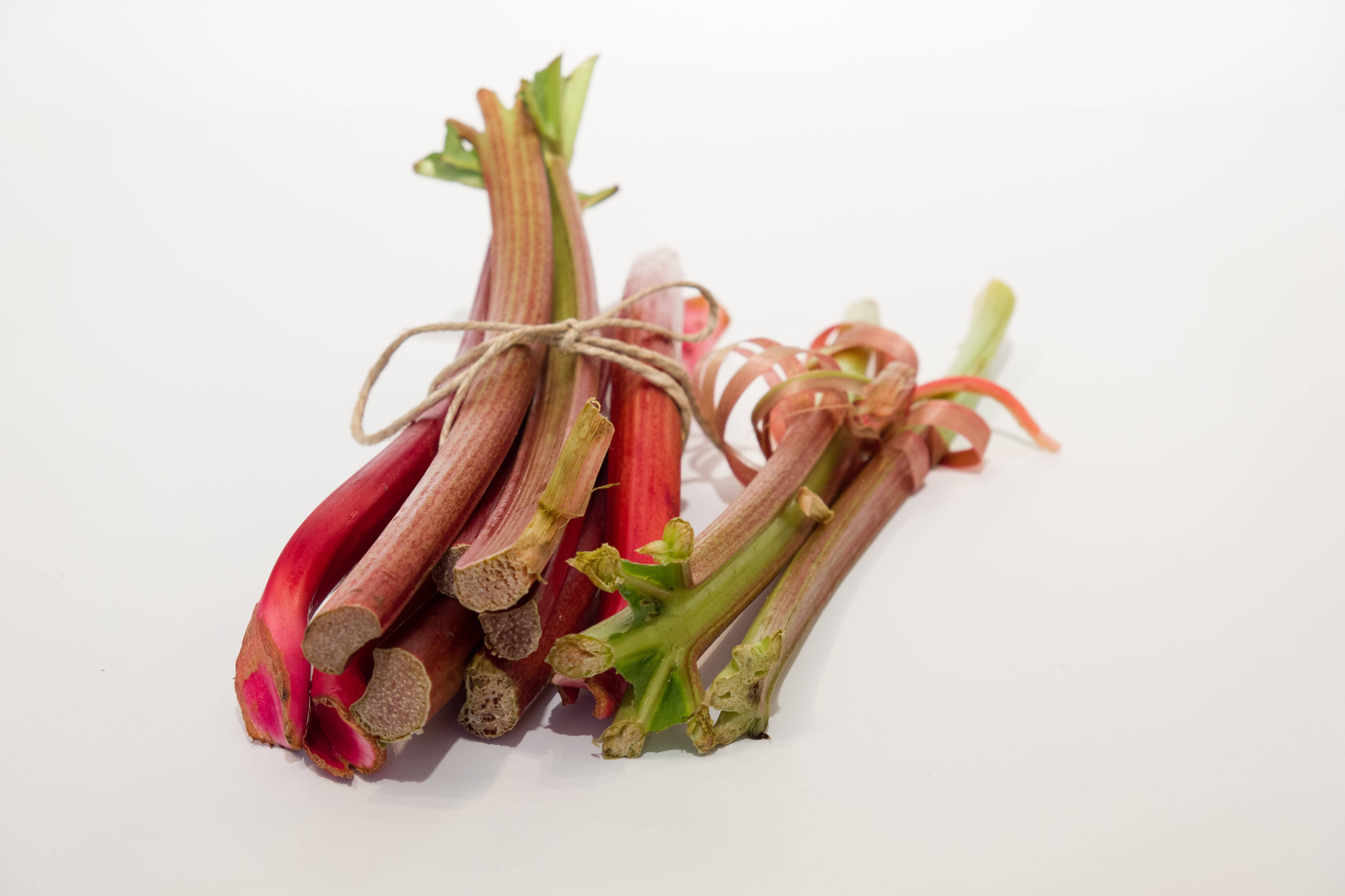 Rhubarb 桌布 壁紙 — 新鮮大黃莖用麻繩捆綁，在純白背景上展現鮮豔的紅色和綠色色調。