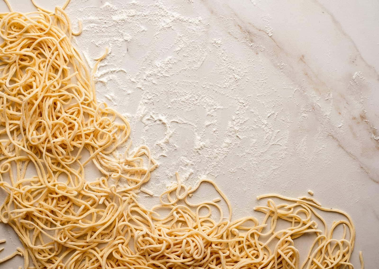 Noodles 桌布 壁紙 — 新鮮手工義大利麵條散落在撒滿麵粉的大理石檯面上。