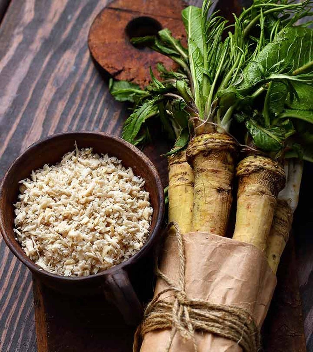 Healthy Food 桌布 壁紙 — 新鮮收穫的辣根根用牛皮紙捆綁，放在深色木質表面上，旁邊有一個木碗裝著磨碎的辣根。