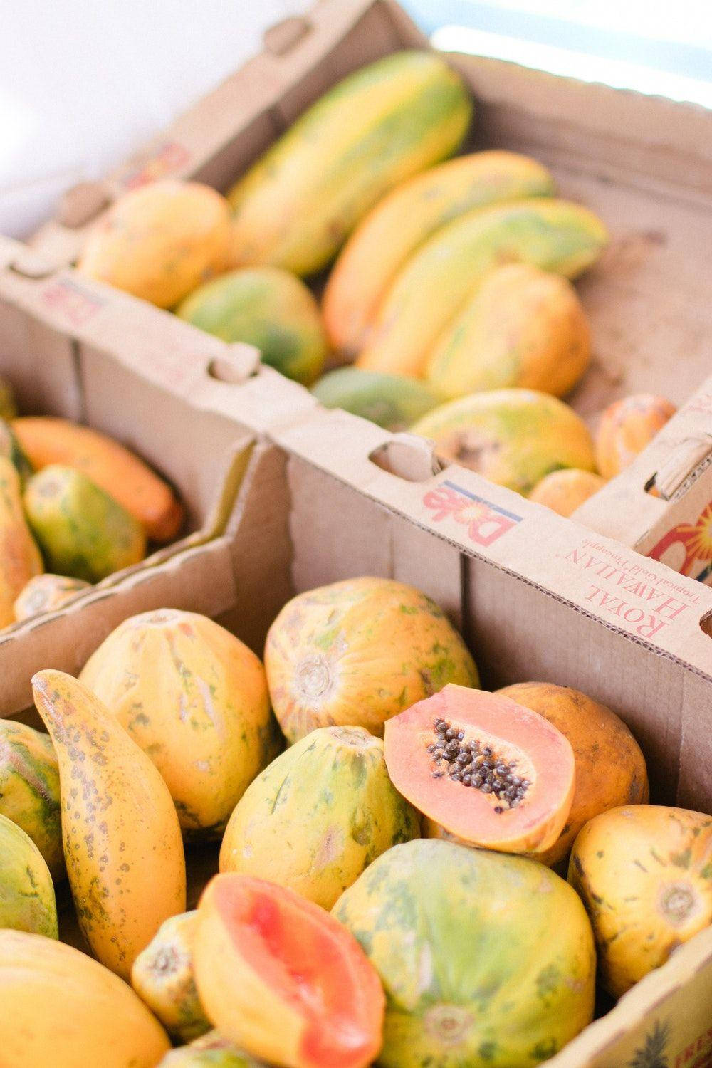 Fruits 桌布 壁紙 — 新鮮木瓜放在紙板箱中，其中一個切開，露出多汁的橙色果肉和黑色種子。