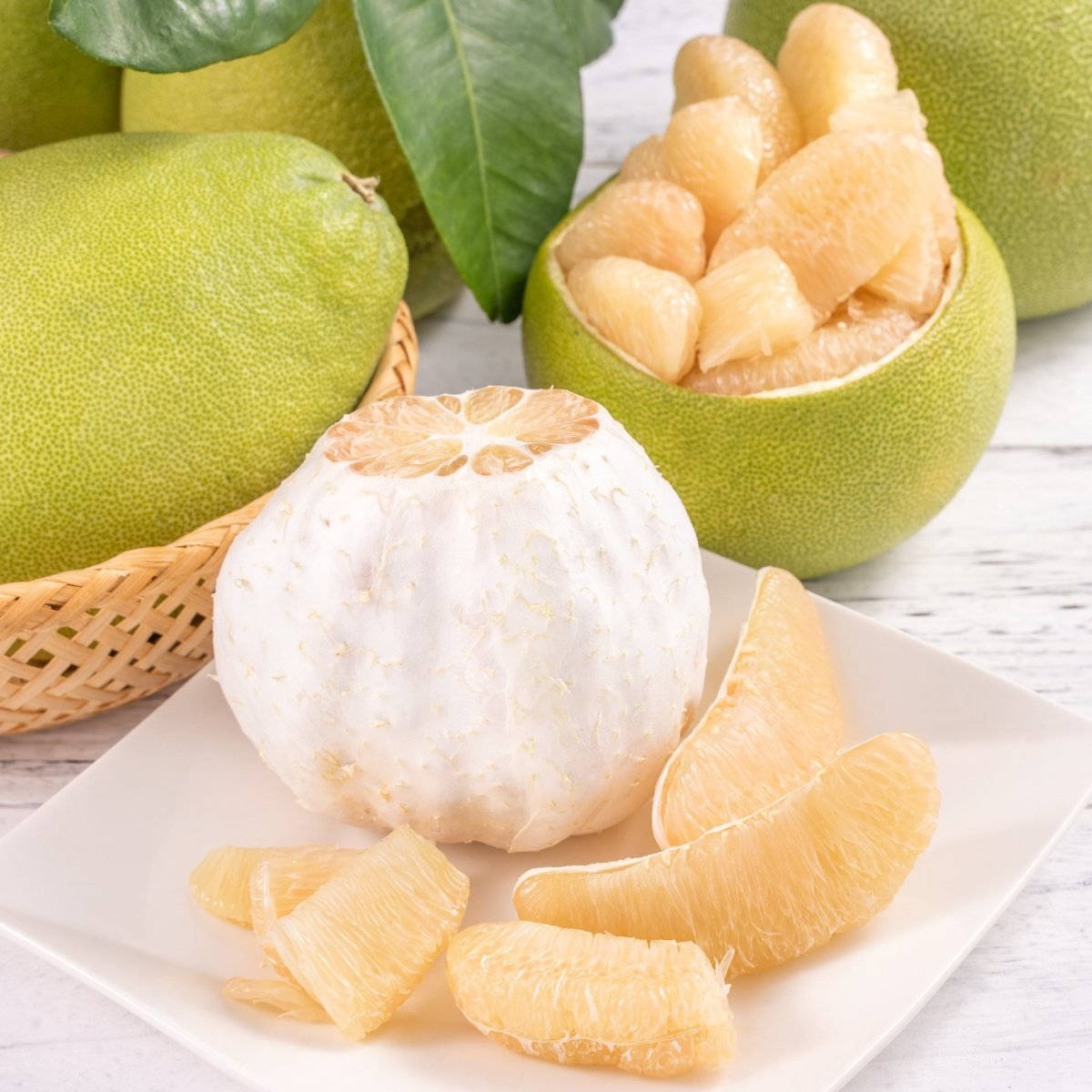 Fruits 桌布 壁紙 — 新鮮柚子，有剝皮果肉和完整果實，擺放在白色盤子上，配上綠葉和編織籃。
