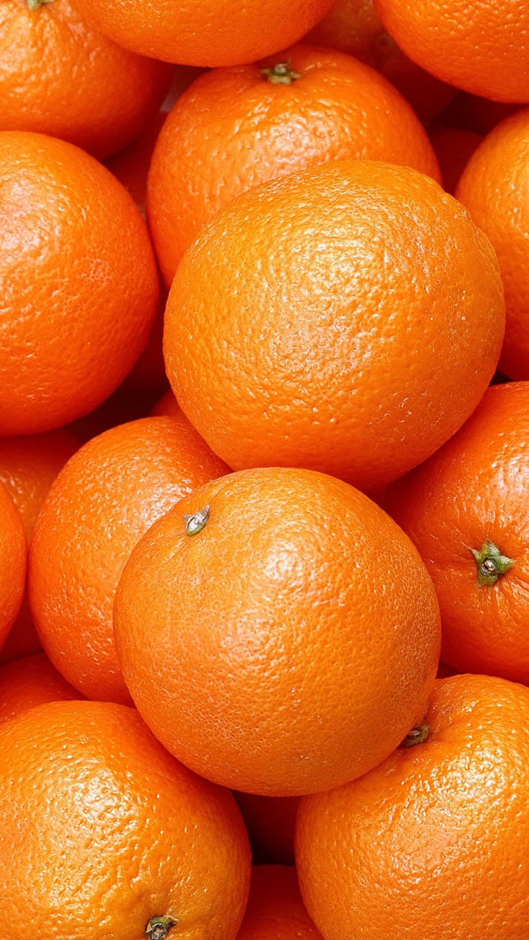 Orange iPhone 桌布 壁紙 — 新鮮柳橙堆疊在一起的鮮明特寫，展示其紋理果皮和明亮的橙色色調。