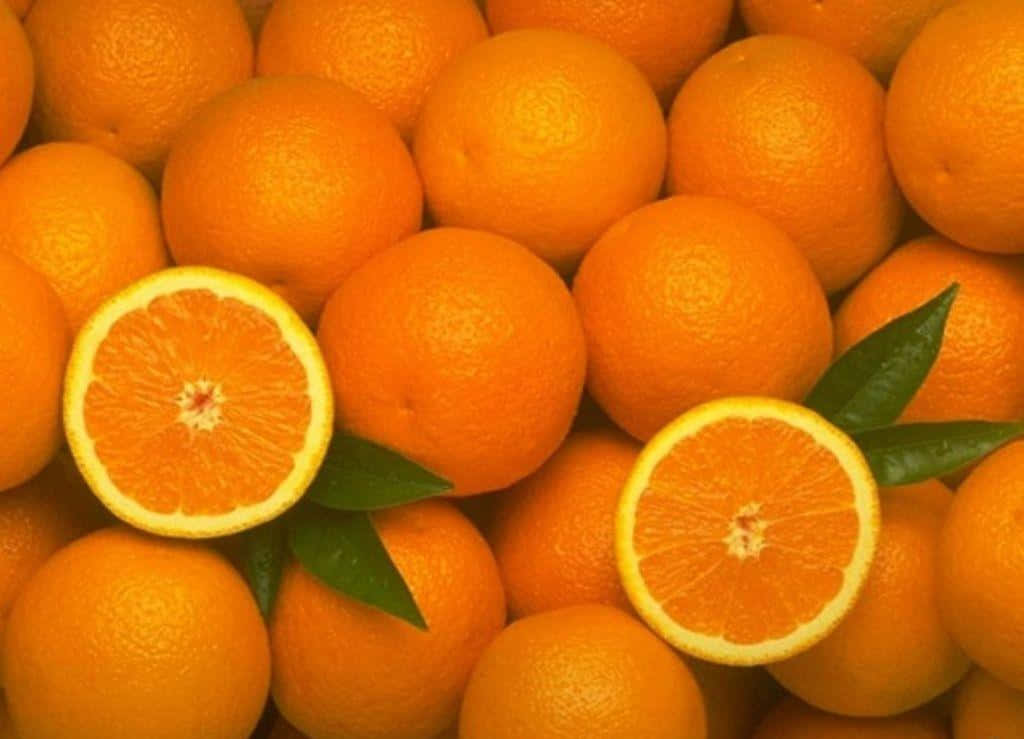Orange Fruit 桌布 壁紙 — 新鮮柳橙的鮮豔特寫，兩個切半的柳橙露出多汁的果瓣，綠色葉子藏在完整水果之間。